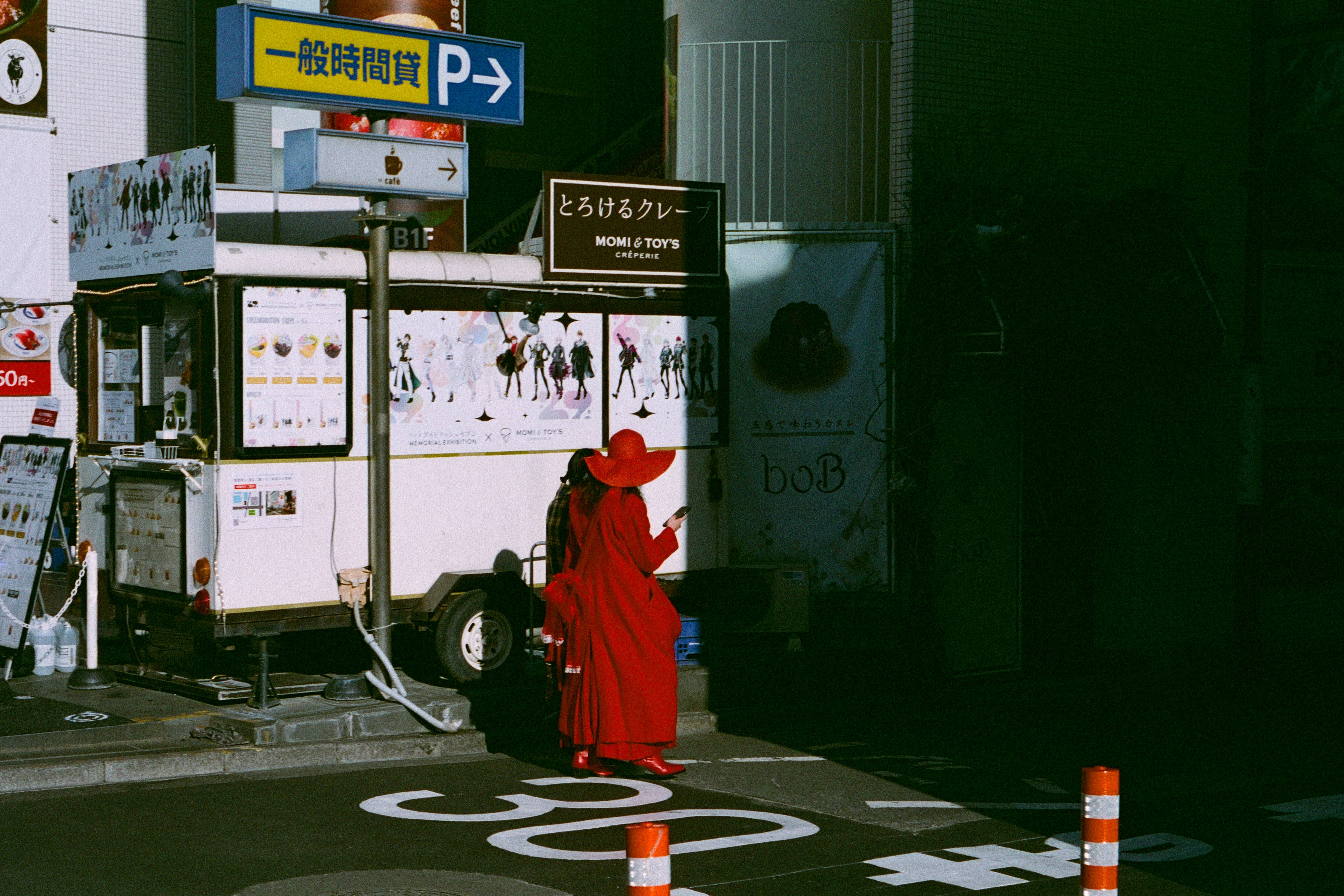 赤いコートの人物が夜の街角の案内板の前に立つ