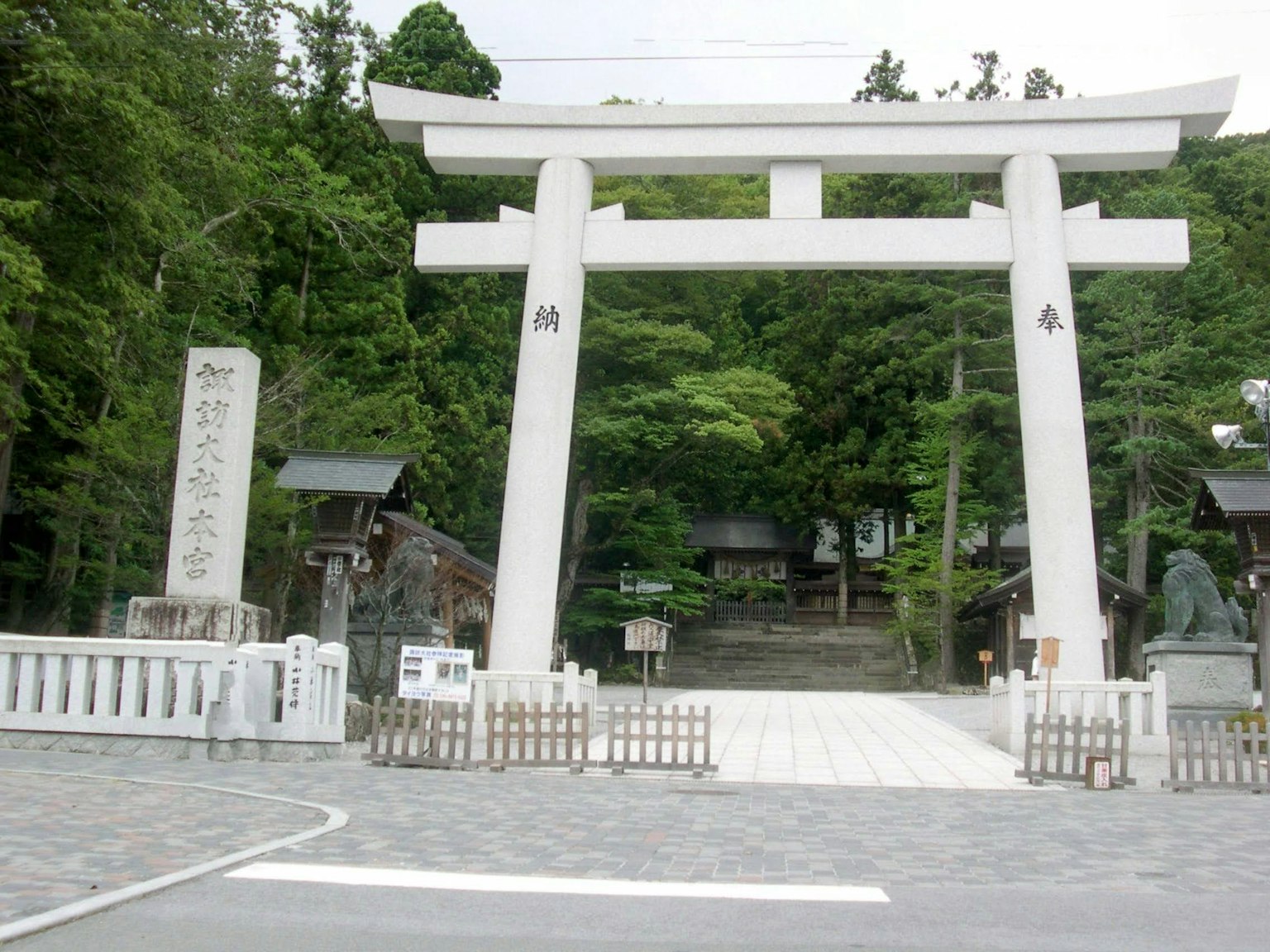 被郁郁蔥蔥的綠樹環繞的神社入口有白色鳥居和石碑