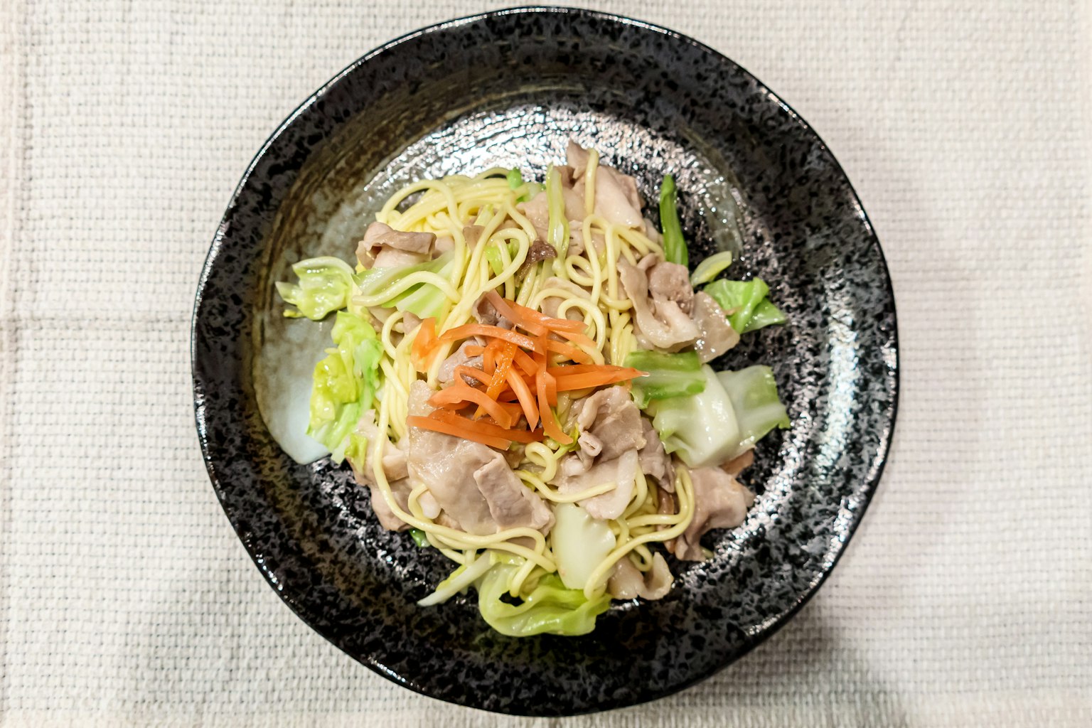 黑碗中的炒麵和蔬菜與豬肉