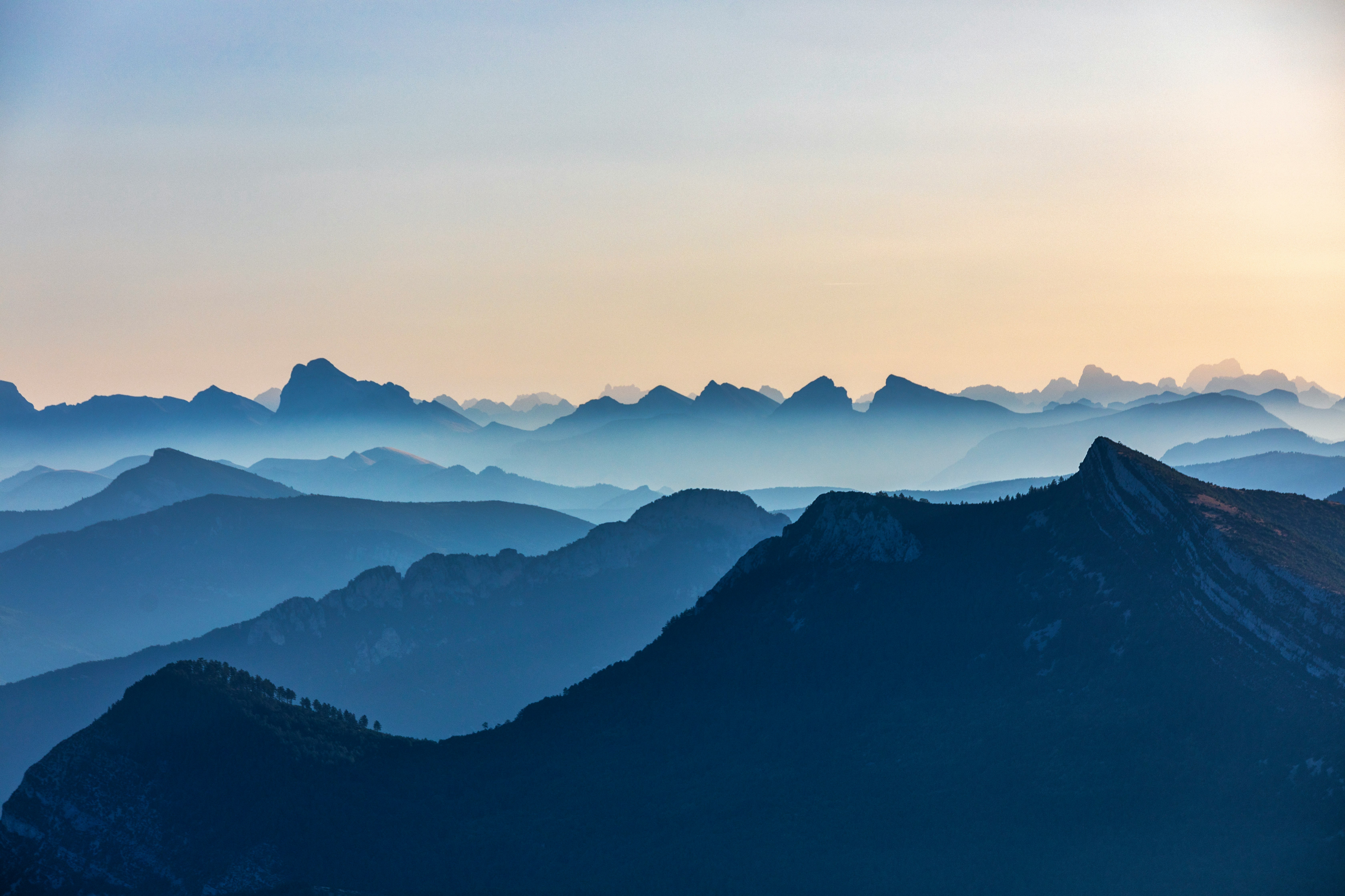 日の出の重なる山並みを望む青とオレンジの空