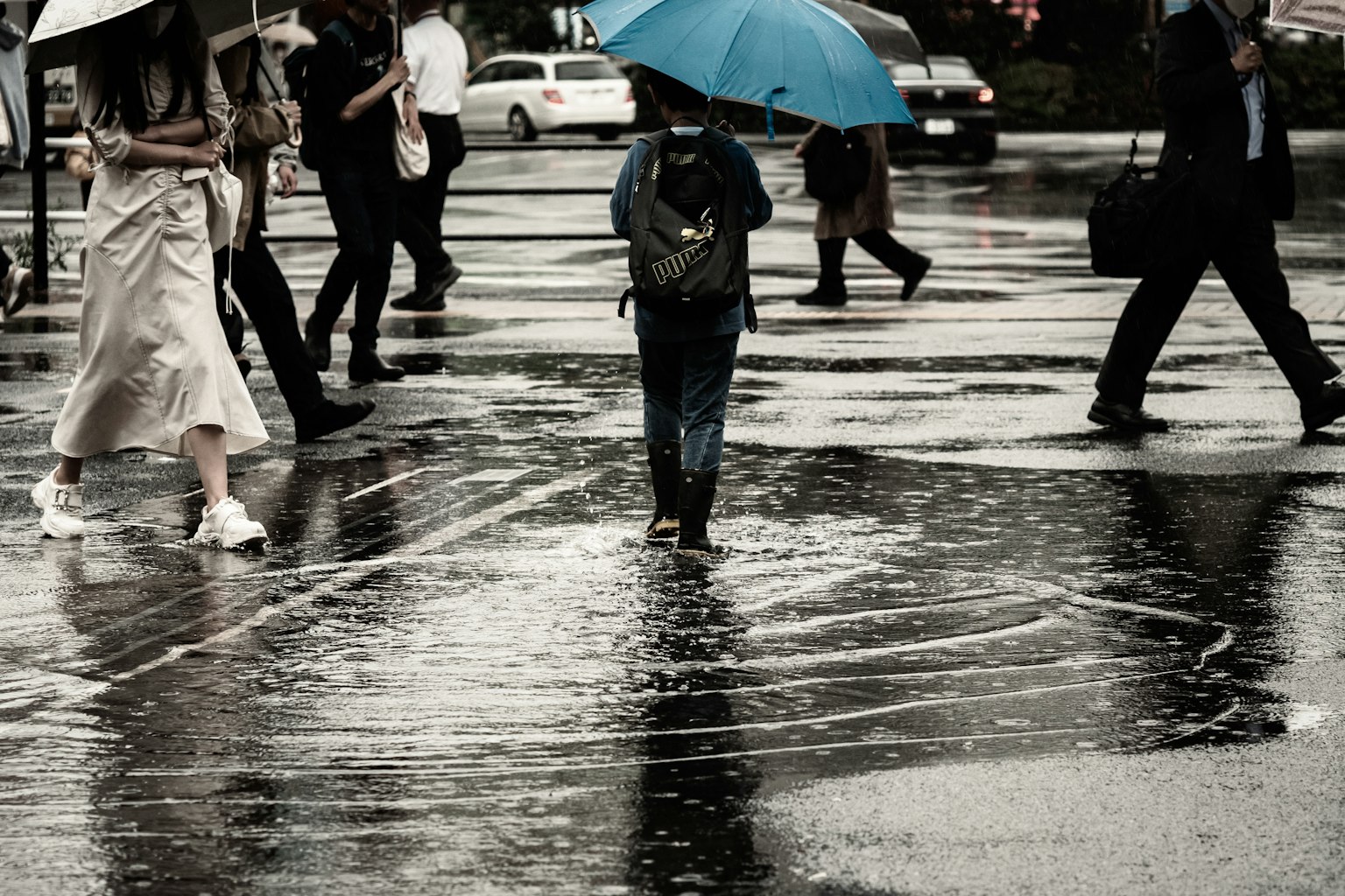 People walking in the rain at a crosswalk with puddles