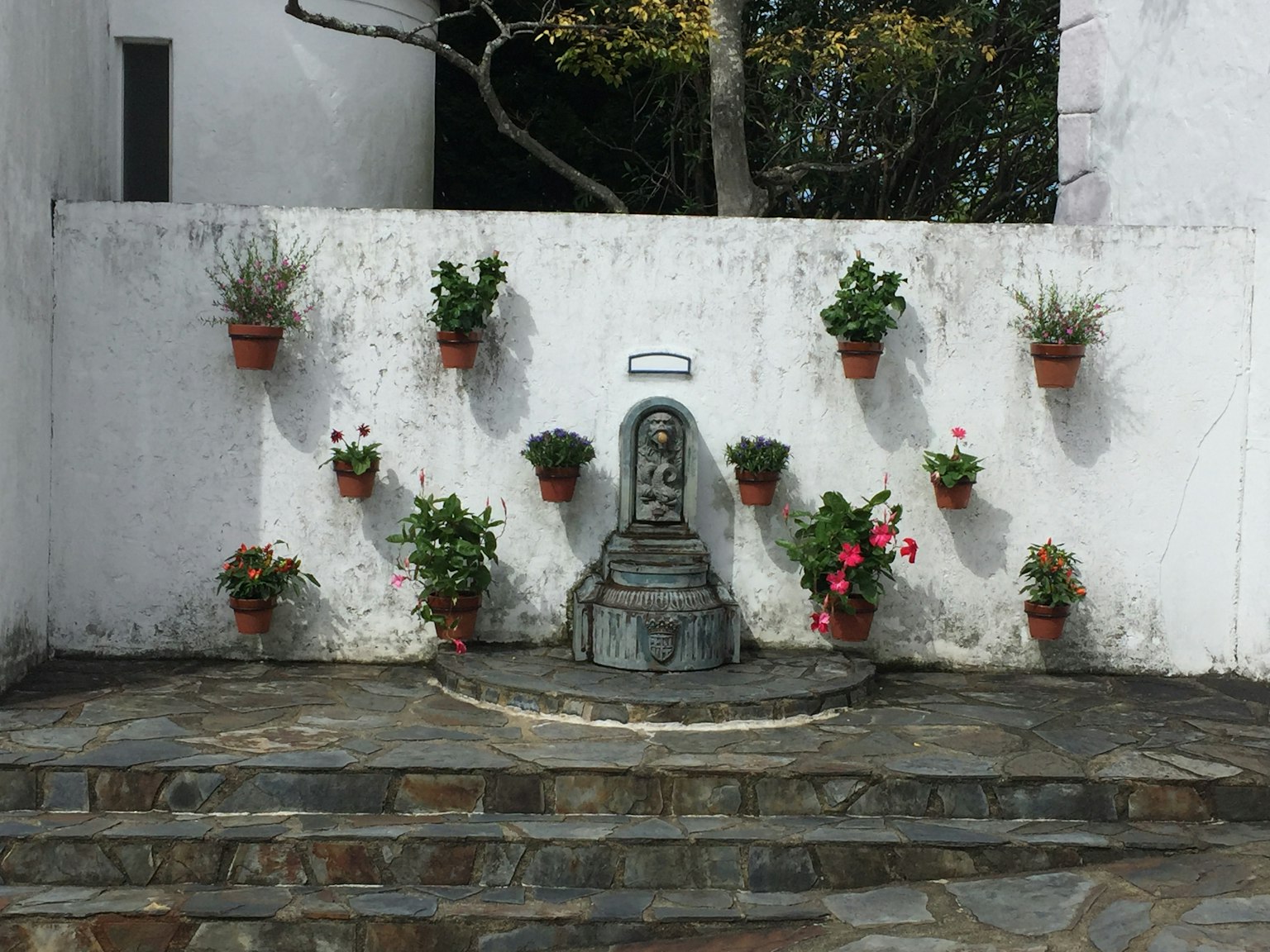 Petit jardin avec une statue en pierre et des pots de fleurs contre un mur blanc