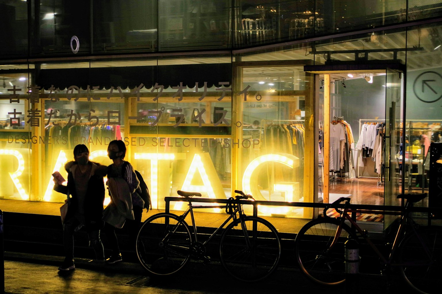 หน้าต่างร้านสว่างในตอนกลางคืนพร้อมคนสองคนและจักรยาน
