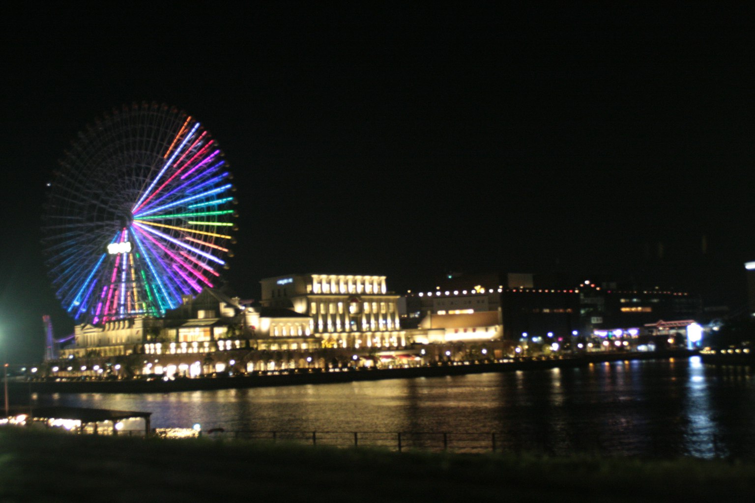 Vista nocturna de una rueda de la fortuna colorida y edificios iluminados