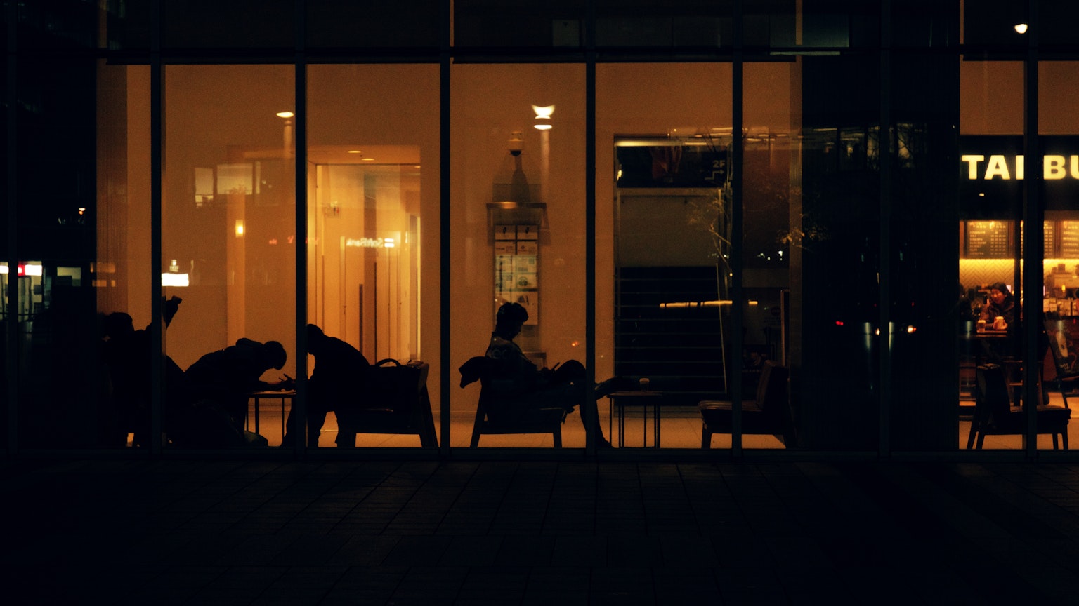 Silhouetten von Menschen, die durch Glaswände mit warmem Innenlicht sichtbar sind