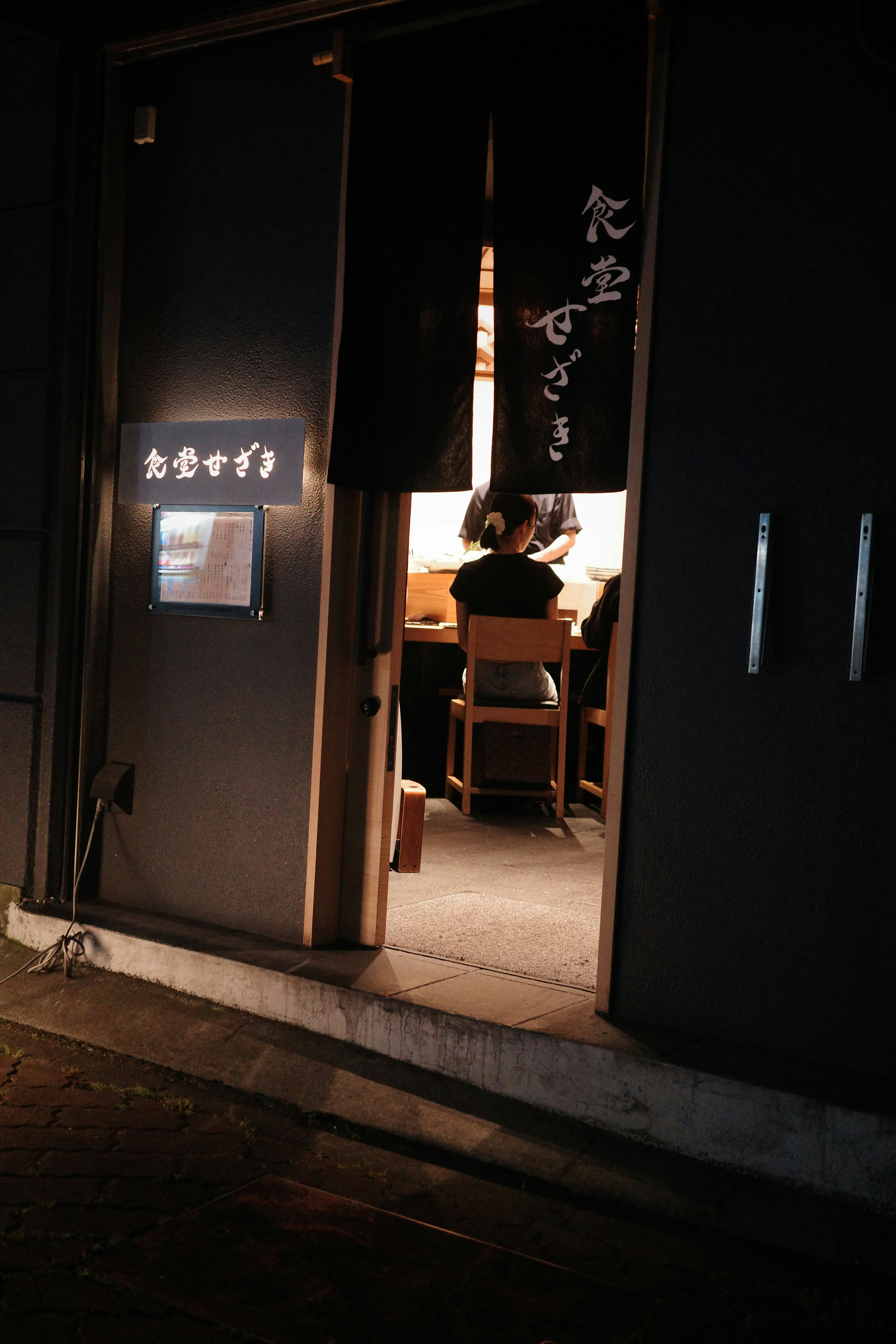 路地の入口からのれんと店内の椅子が見える和風飲食店の夜景