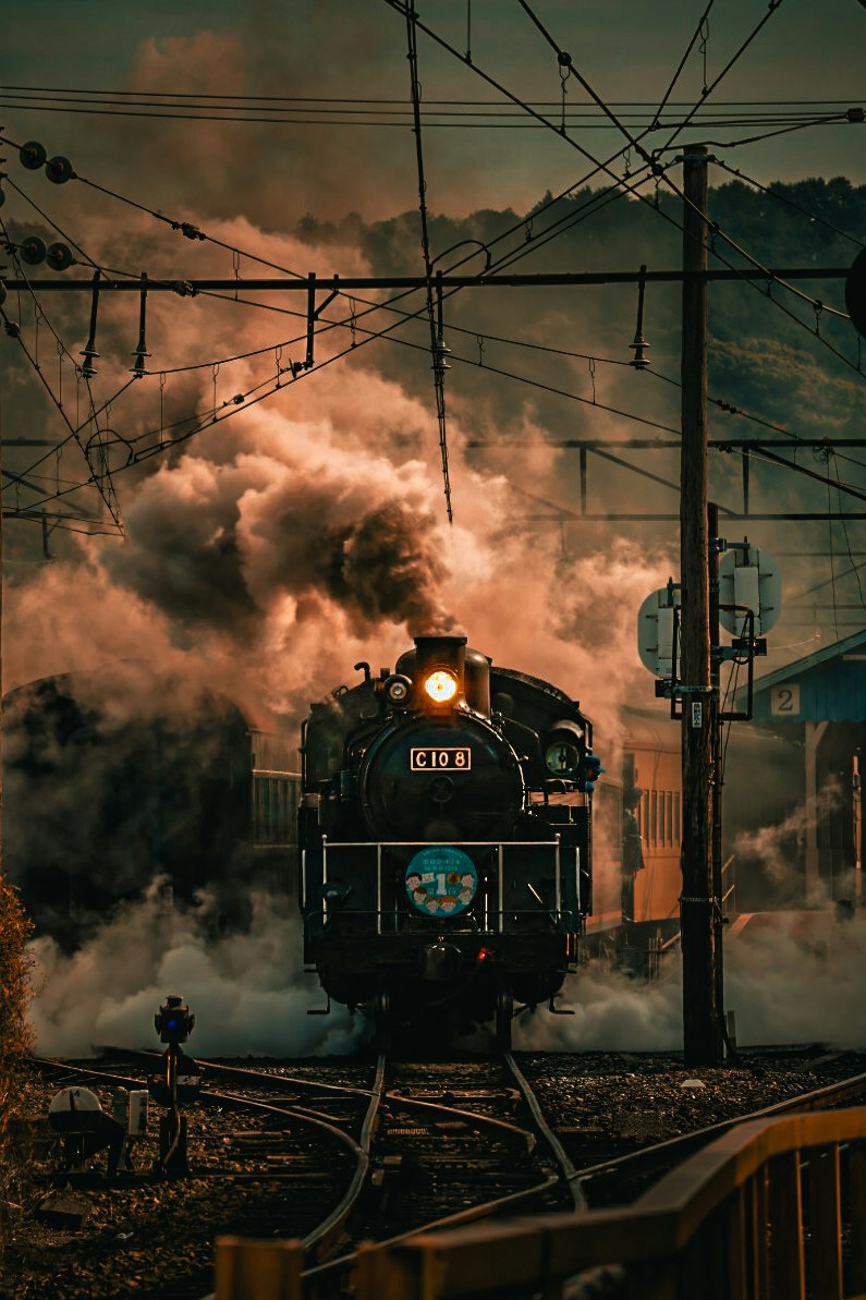 steam locomotive moving along tracks through heavy smoke at dusk