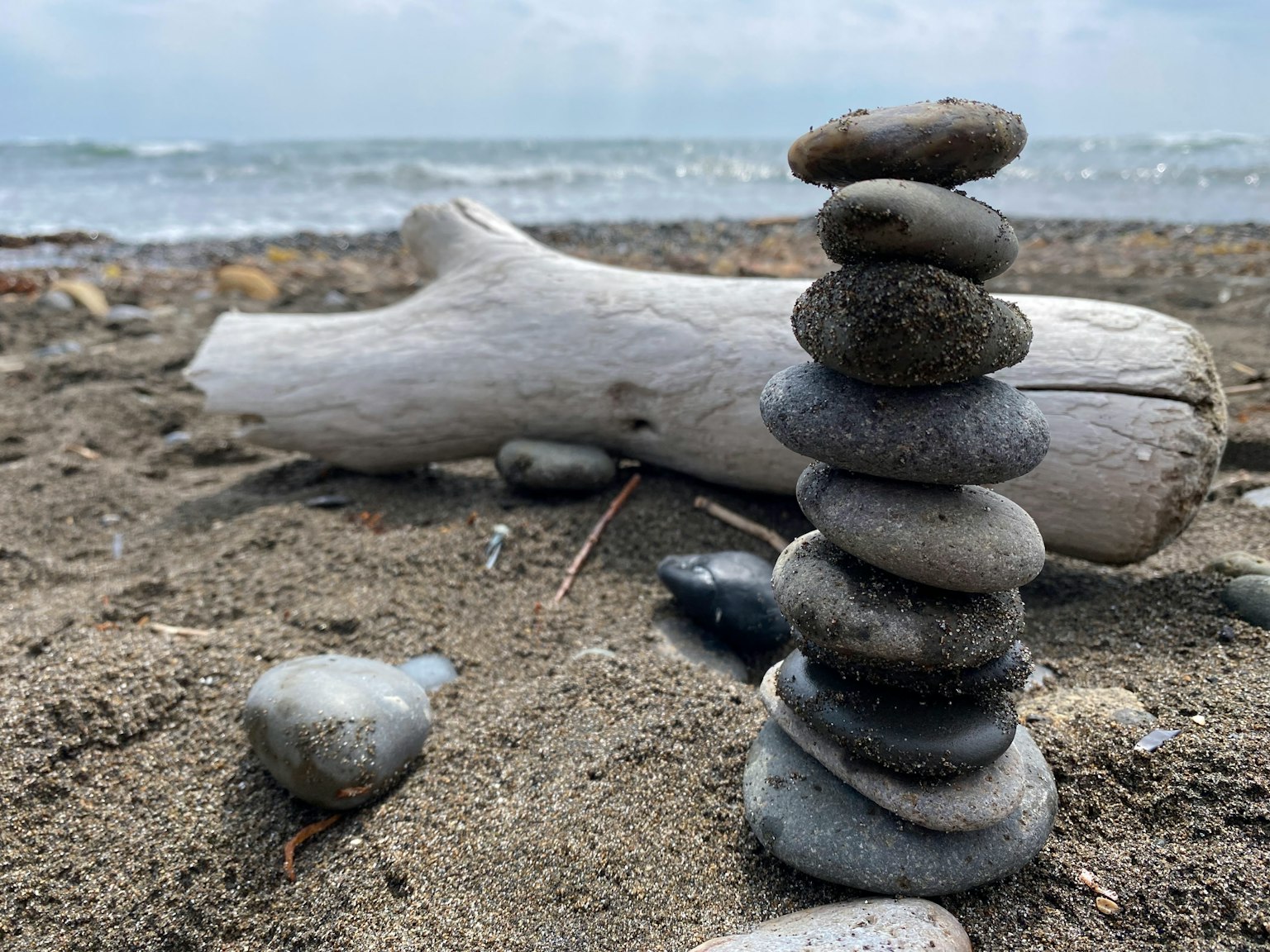 Una pila di pietre lisce sulla spiaggia con legno flottante sullo sfondo