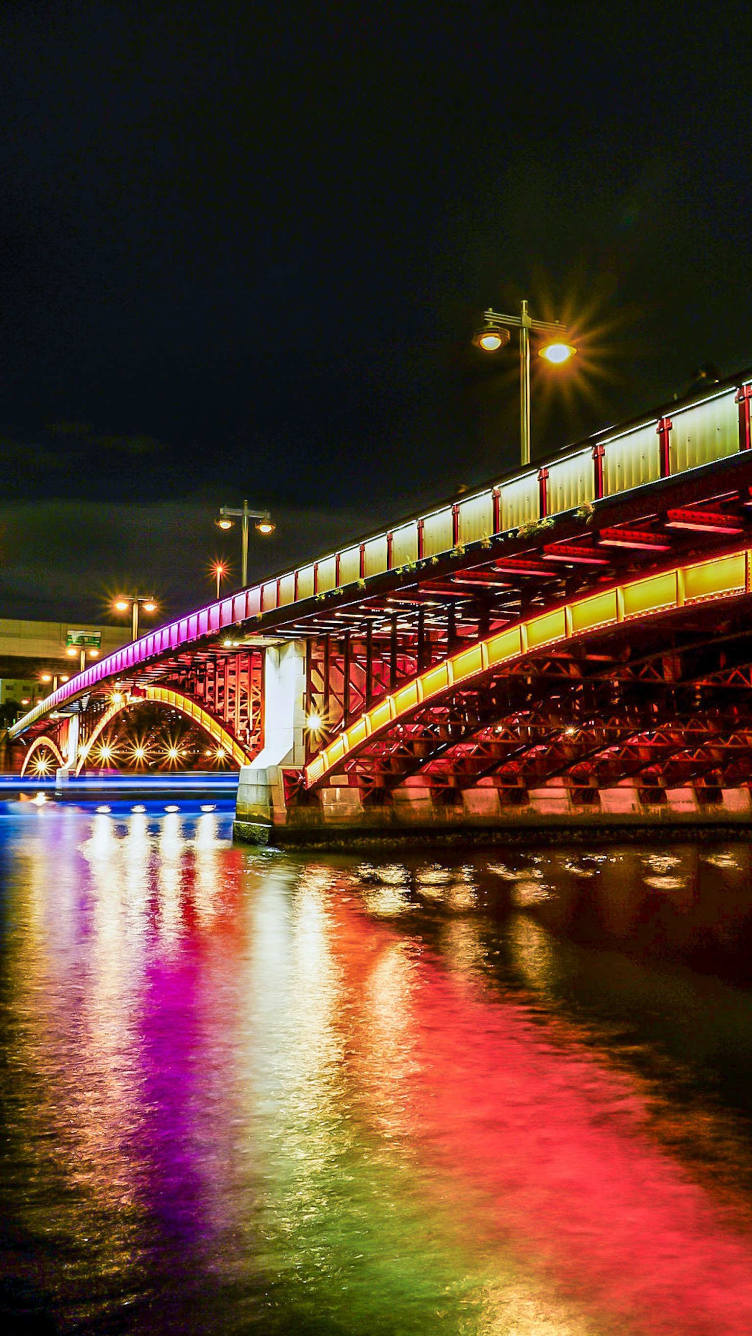 สะพานที่มีสีสันสว่างในตอนกลางคืนกับการสะท้อนบนผิวน้ำ