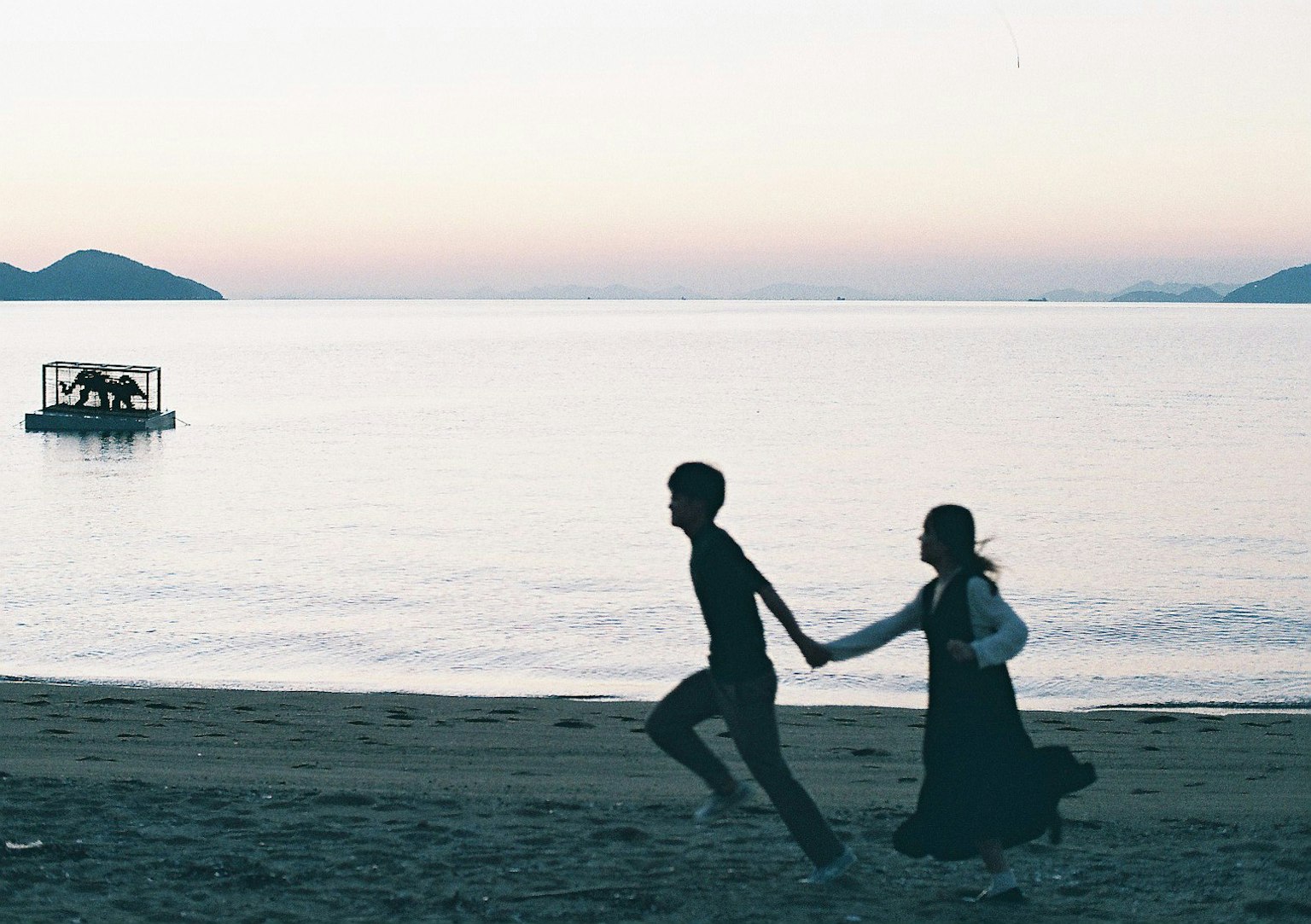 Silhouette eines Paares, das Hand in Hand am Strand bei Dämmerung läuft