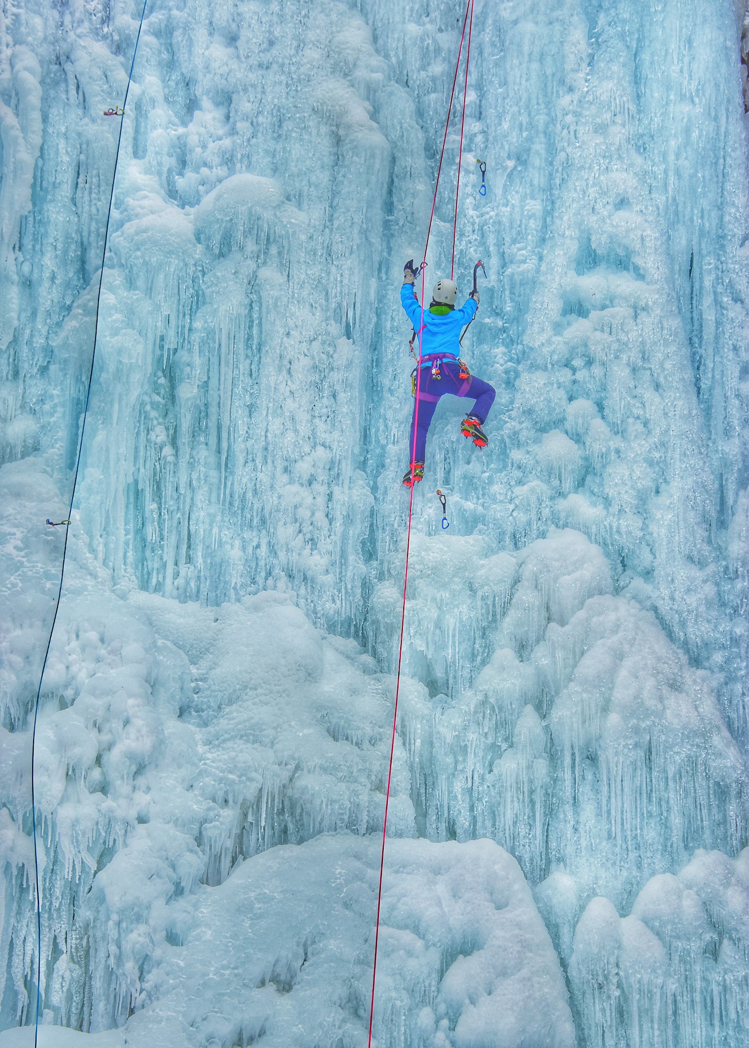 Kletterer in blauer Kleidung und lila Hose, der eine Eiswand erklimmt