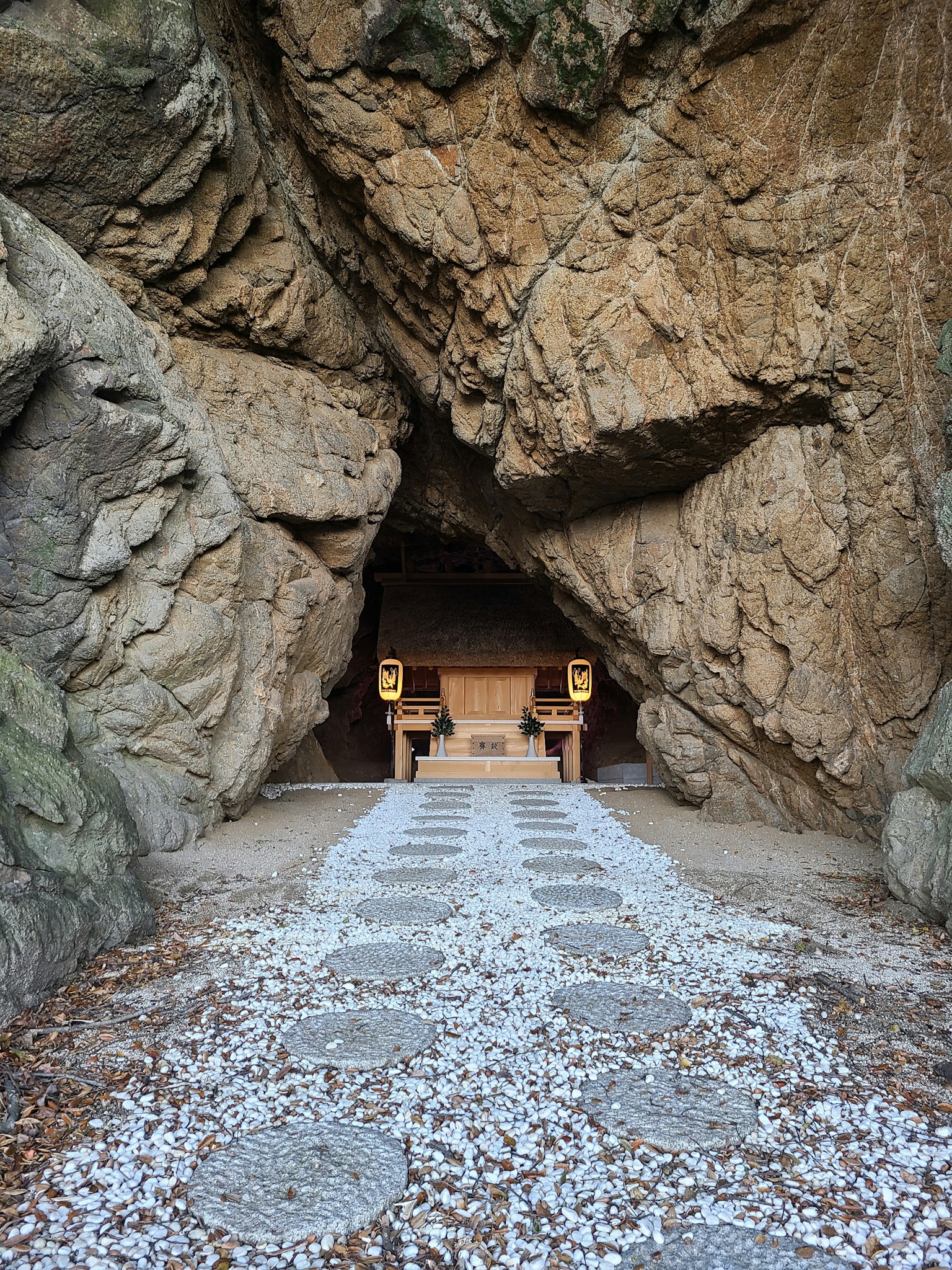 Entrance of a shrine nestled between rocks with stone path and white gravel
