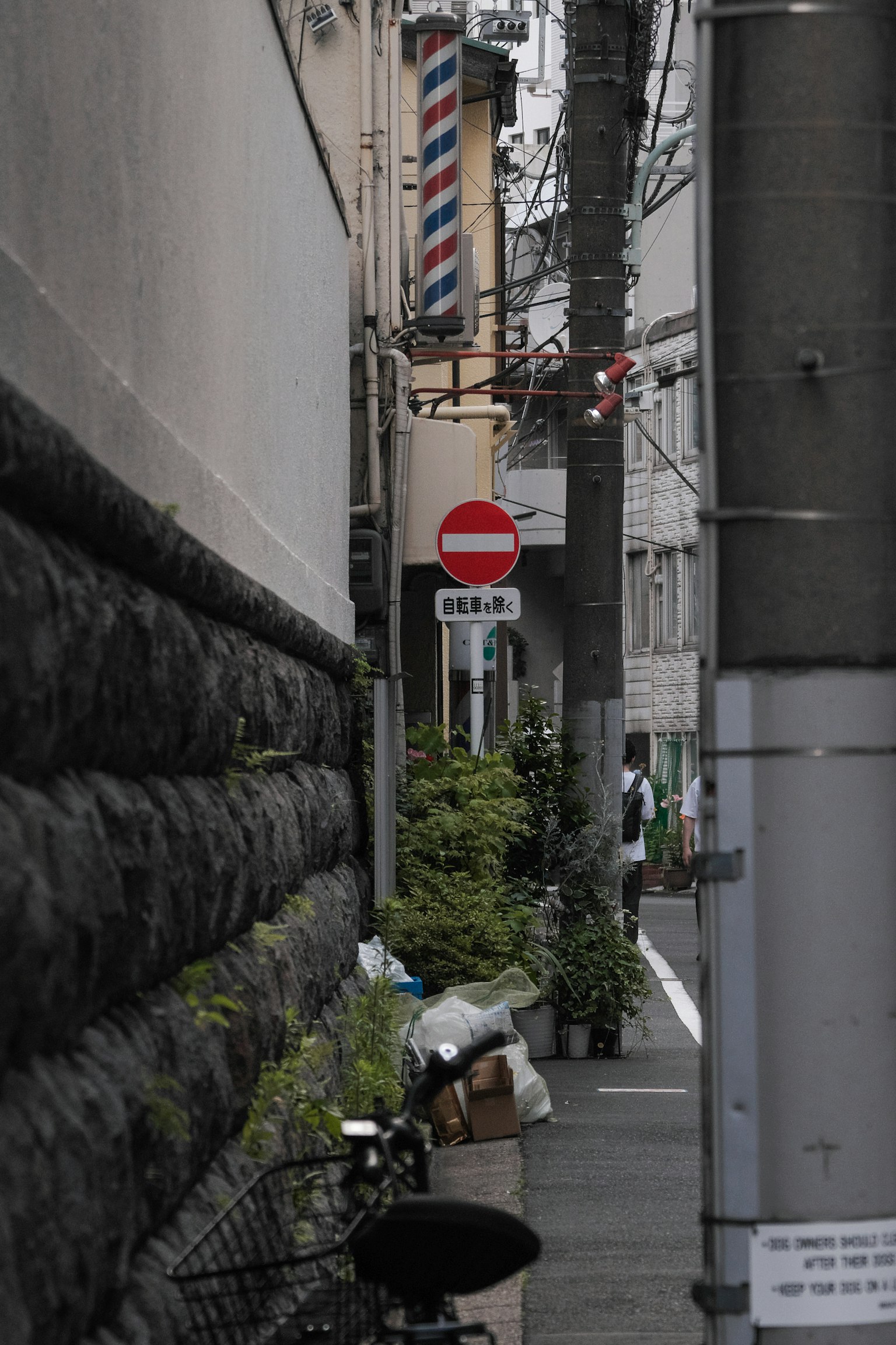 Narrow alley featuring a barber shop sign and a no entry sign with surrounding plants