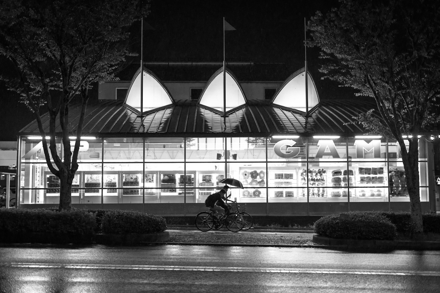 Une personne à vélo avec un parapluie la nuit devant un bâtiment lumineux