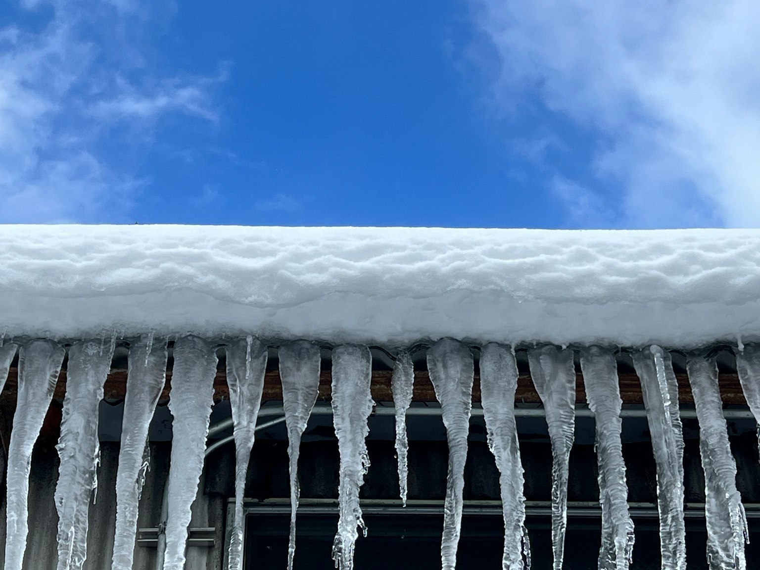 Eiszapfen hängen von einem schneebedeckten Dach vor blauem Himmel