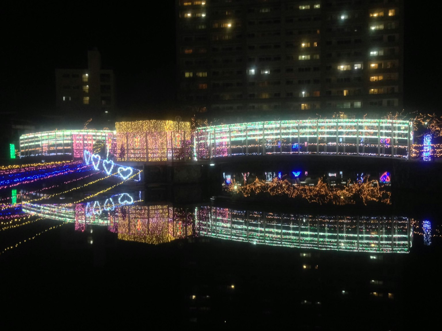 Bunte Lichter, die sich nachts im Fluss spiegeln, mit herzförmigen Dekorationen an der Brücke