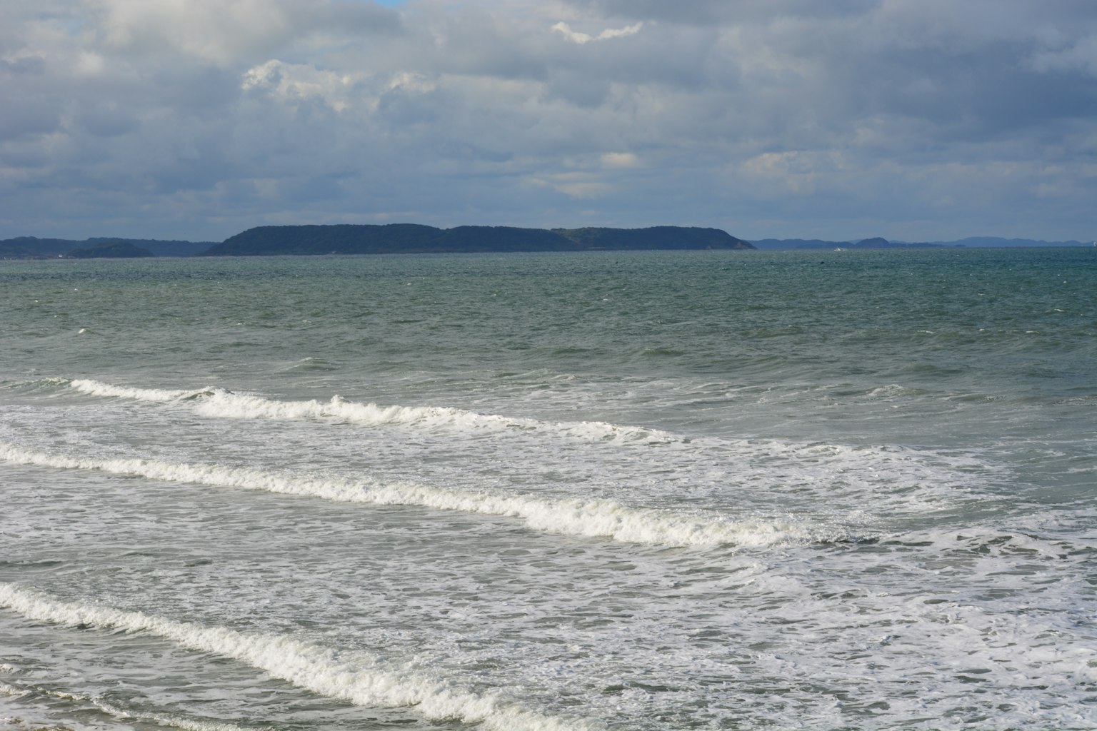 Waves on the sea under a cloudy sky with an island in the distance