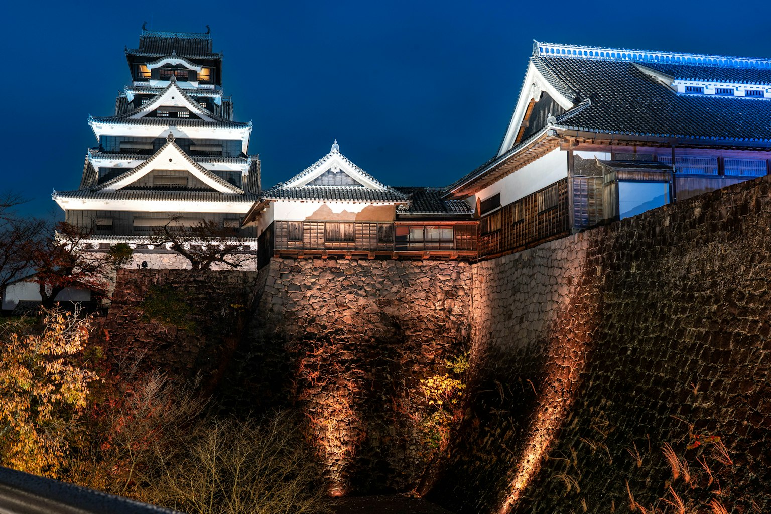 ด้านนอกที่สวยงามของปราสาทคุมะโมโตะในยามค่ำคืนพร้อมกำแพงหิน
