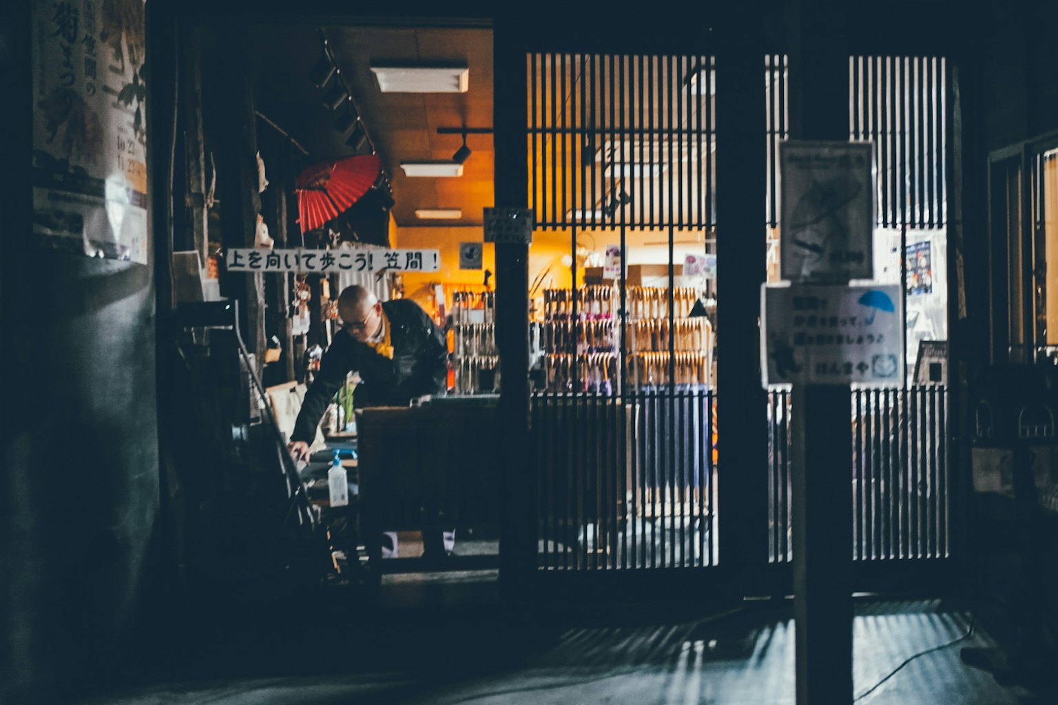 ภายนอกของร้านหนังสือที่มีแสงไฟอุ่นอยู่ข้างใน คนทำงานที่เคาน์เตอร์