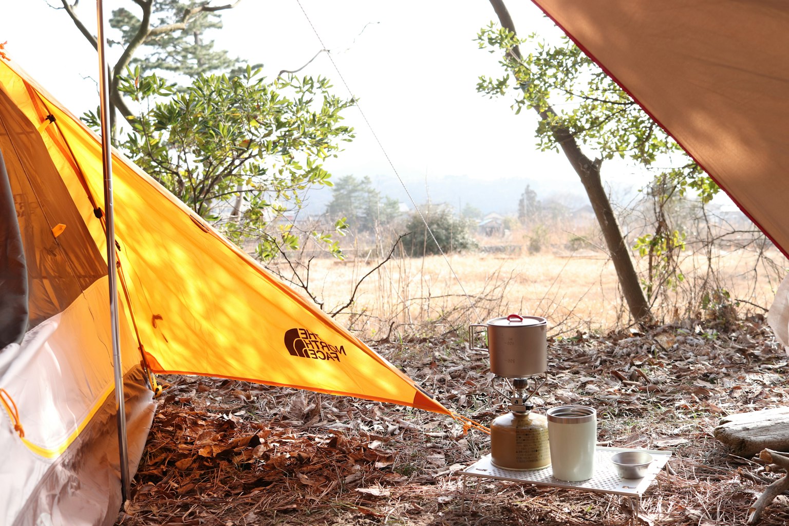 Pemandangan berkemah dengan tenda oranye dan kompor camping