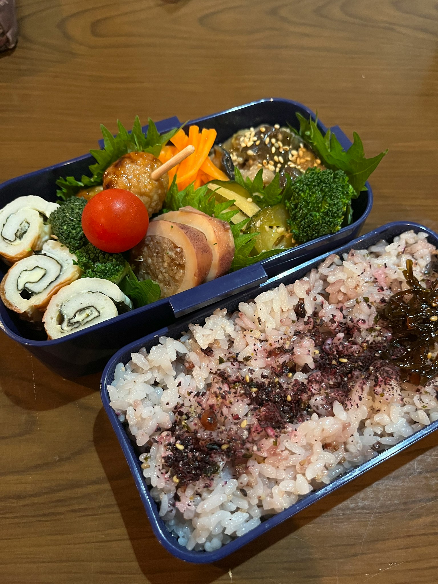 一个便当盒里装满了各种颜色的食材，包括寿司卷、蔬菜和米饭