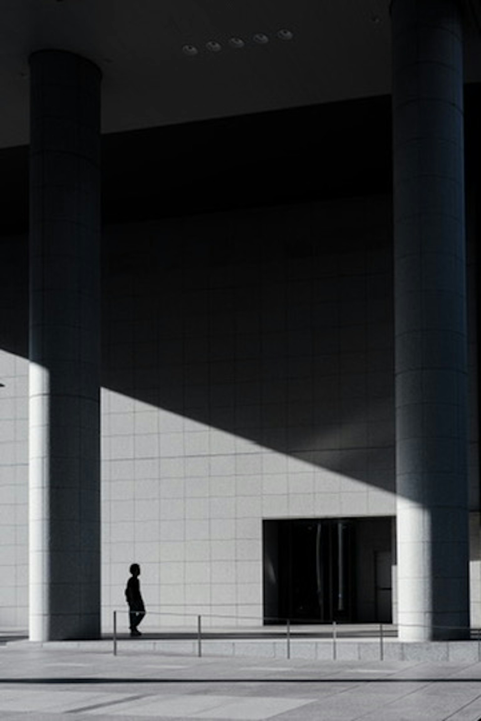 Fachada moderna de un edificio con sombras y luces cruzadas que presenta a una persona en silueta