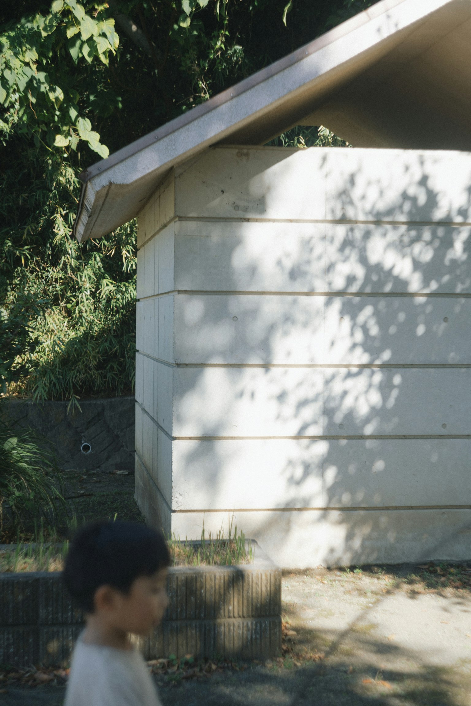 子供が歩いている白い建物の横に影が映る風景