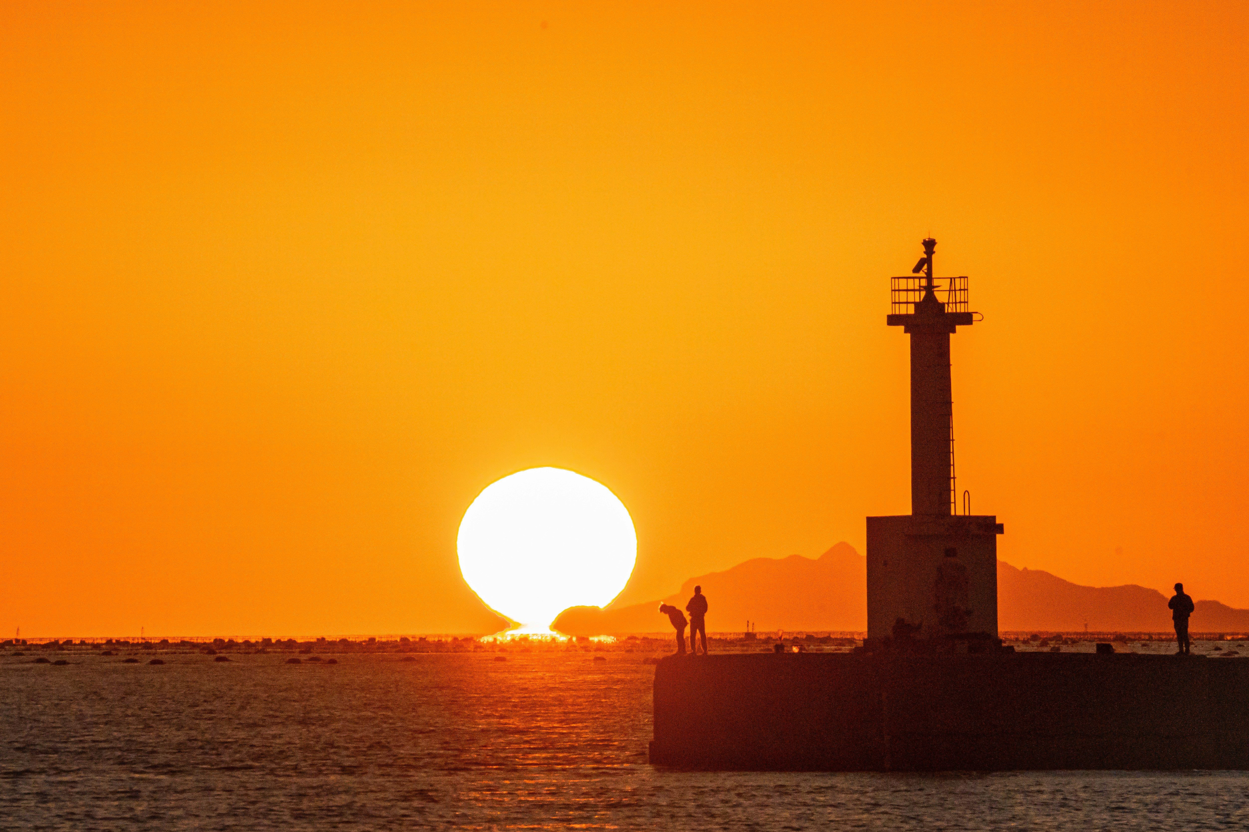 夕日に照らされた海辺の灯台と水平線