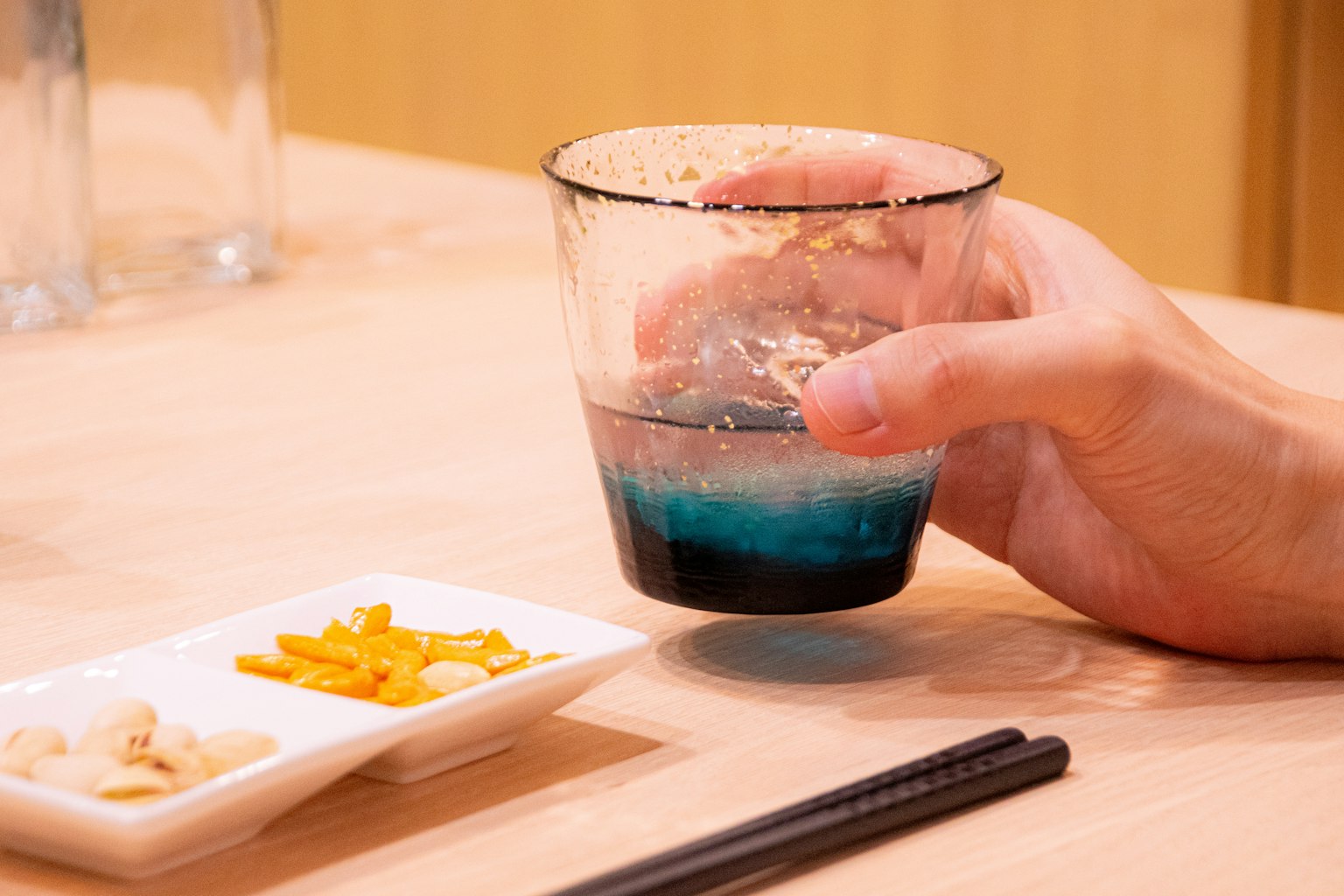 手握著裝有藍色飲料的杯子，旁邊有一盤小吃