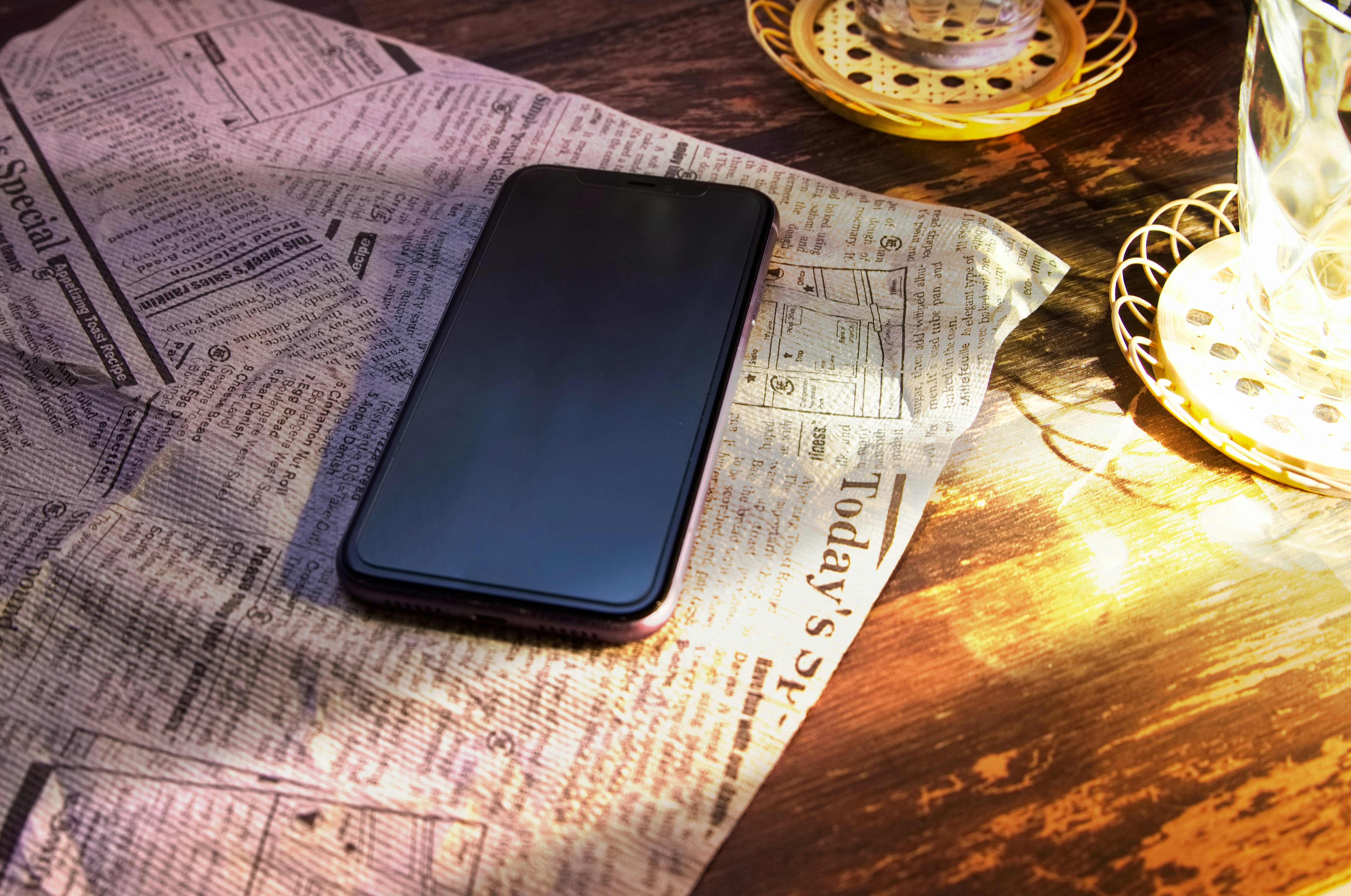 smartphone di atas koran dengan kopi di atas meja kayu