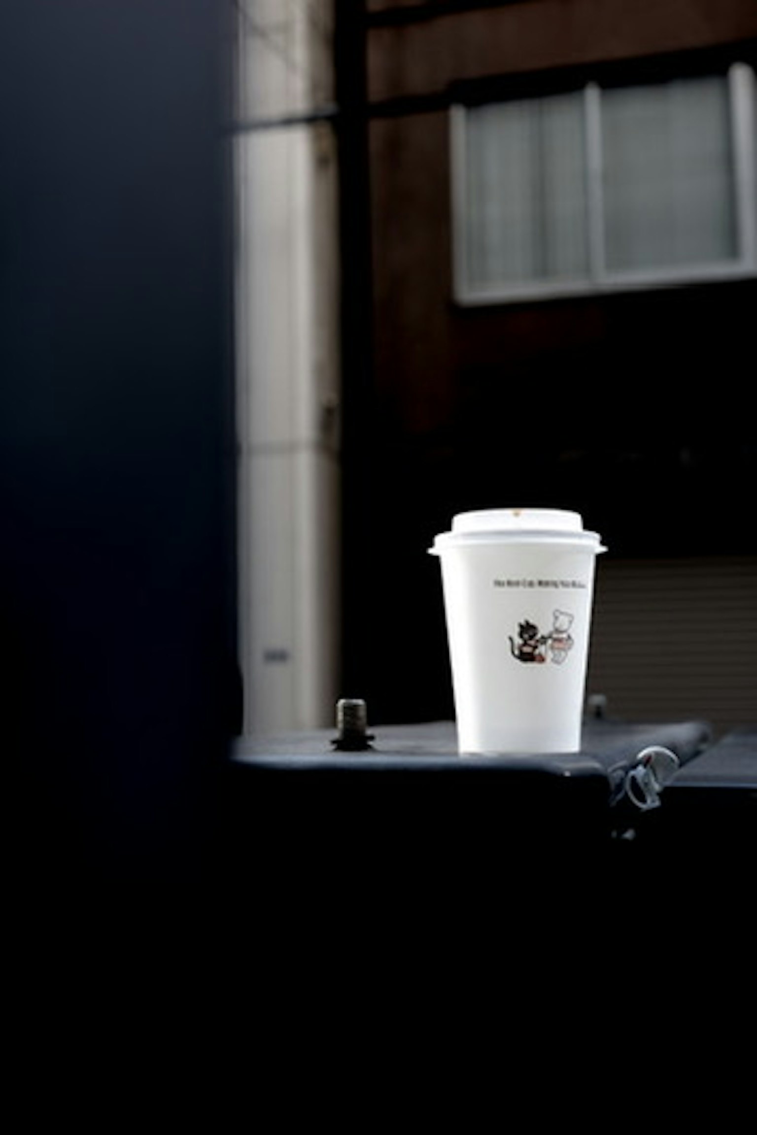 ถ้วยกาแฟสีขาววางอยู่บนพื้นผิวสีเข้มพร้อมอาคารเบลออยู่เบื้องหลัง