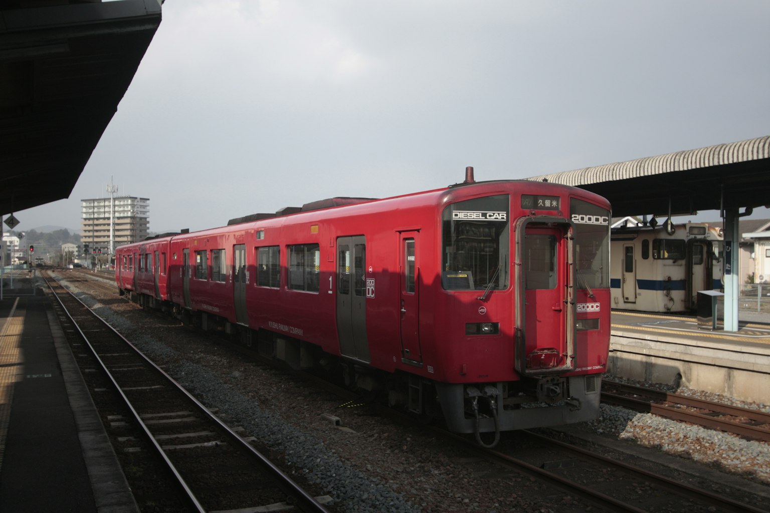 Red train parked at a station with a cloudy sky