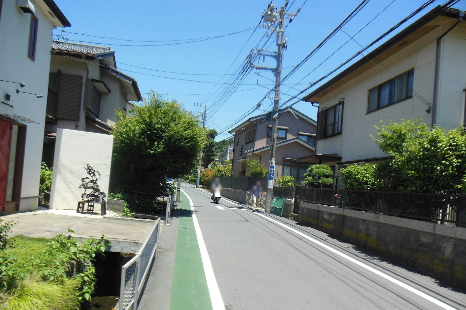 Quiet residential street with a green bicycle lane houses and power lines visible