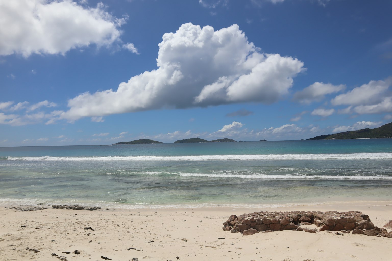 Scenic view of blue ocean and white sandy beach with large clouds in the sky