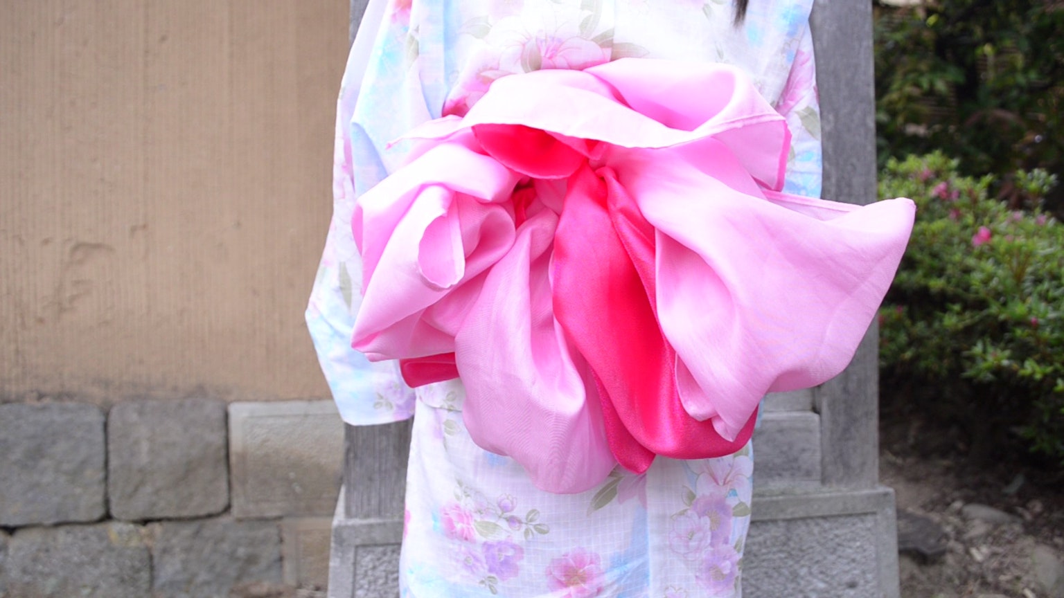 Seorang wanita dalam kimono memegang obi besar berwarna pink