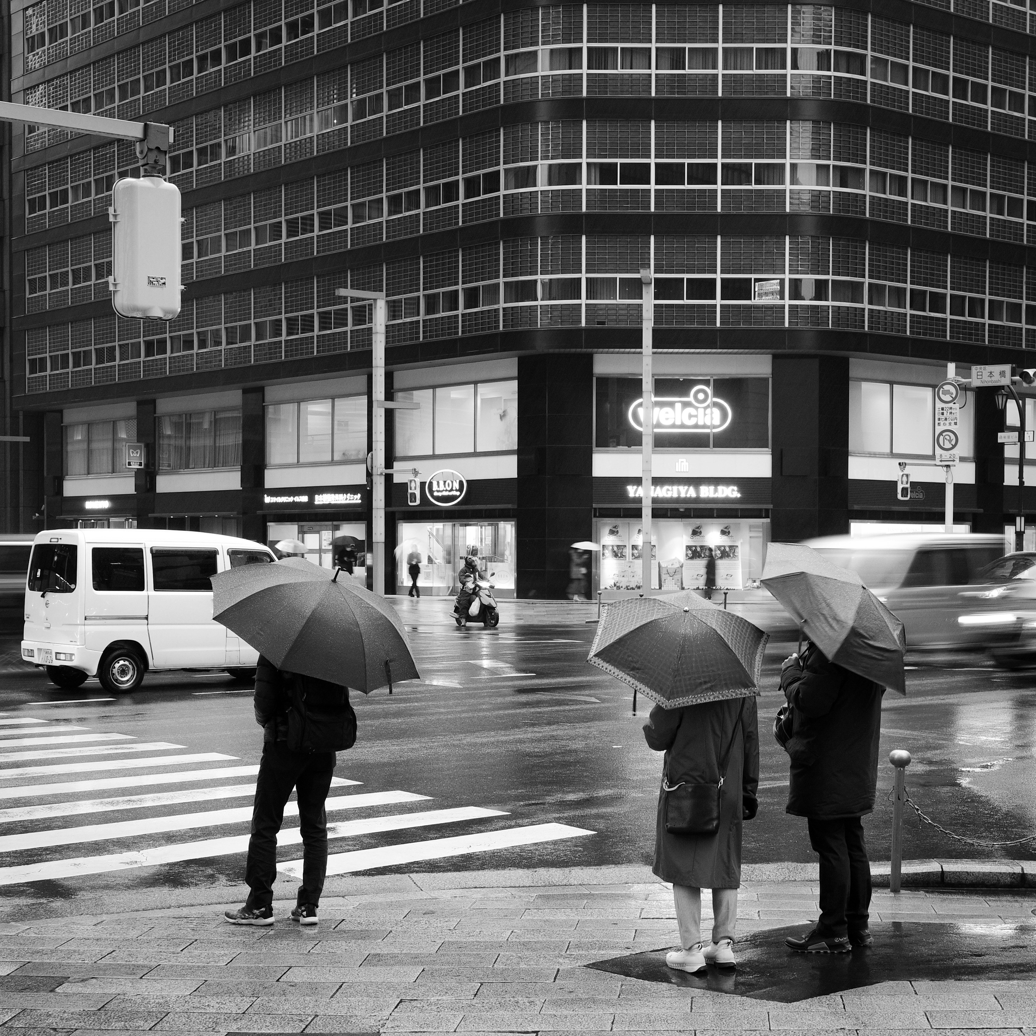 雨の交差点で傘をさす人々と横断歩道のある街角