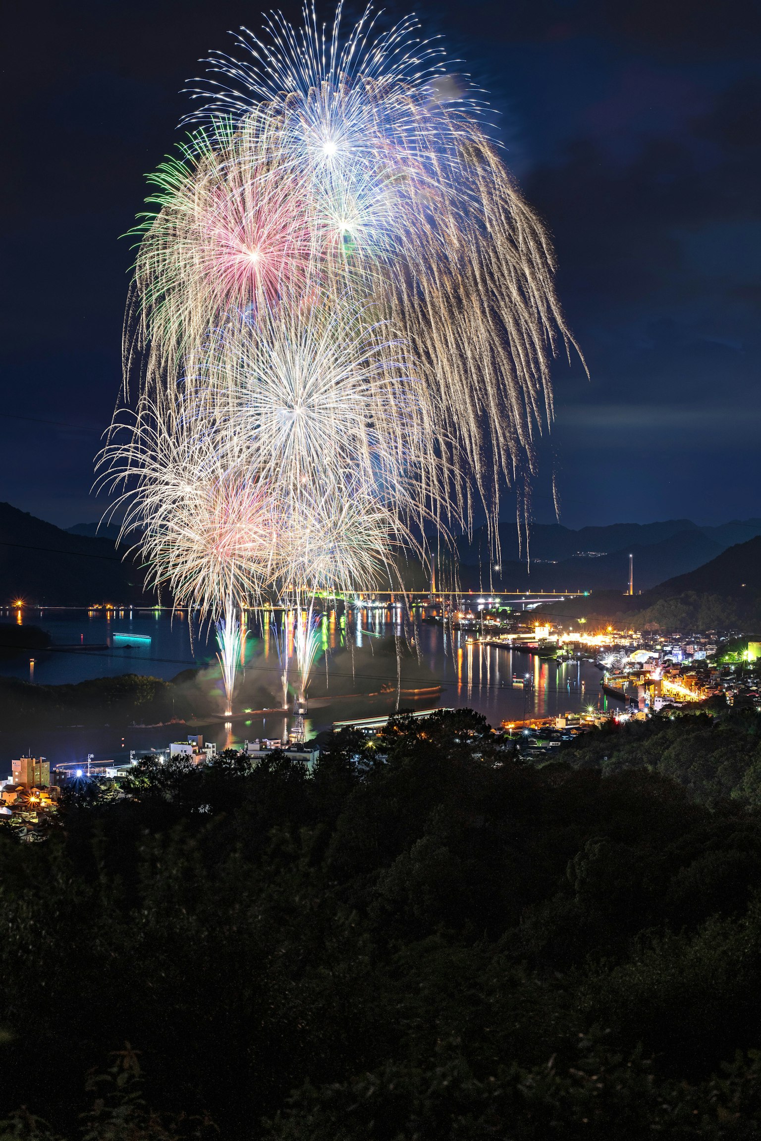 Colorful fireworks bursting in the night sky over a serene waterfront