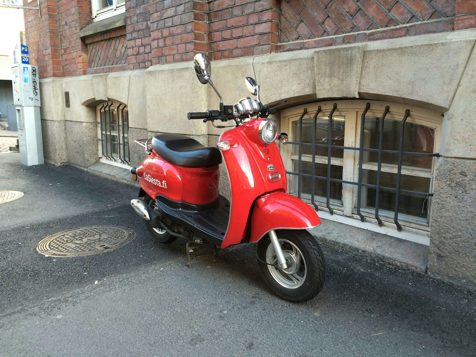 A red scooter parked beside a brick wall