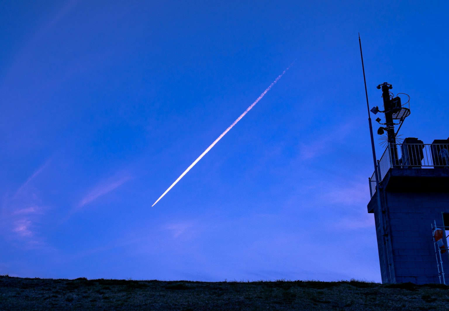 Silhouette of a building with a contrail in the blue sky