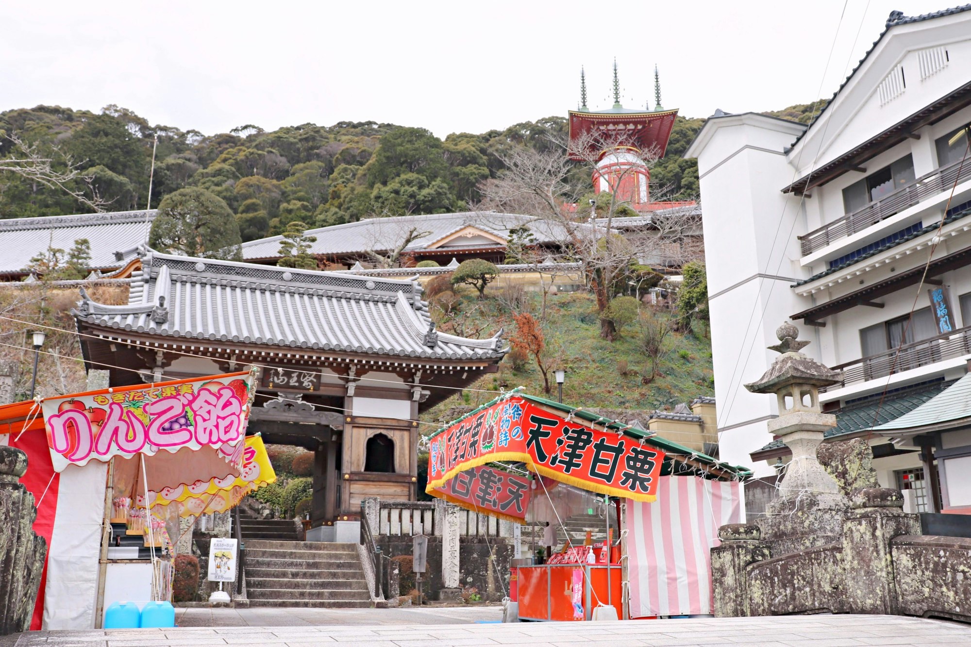 坂道に面した寺院の門と提灯、商店ののれんが並ぶ参道の風景