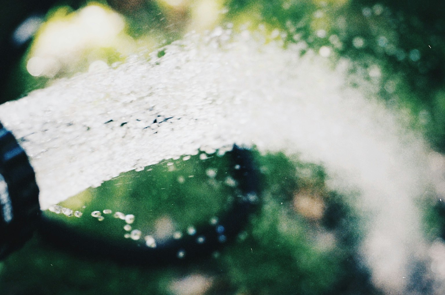Close-up of a hose spraying water against a green background