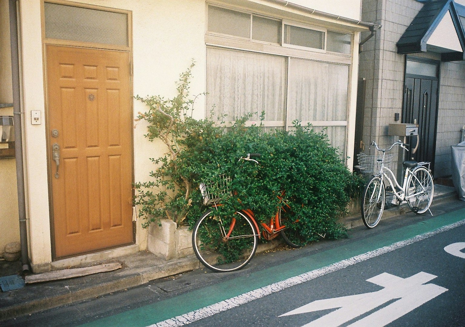 オレンジ色の自転車が緑の植物に囲まれた日本の街並みの一角