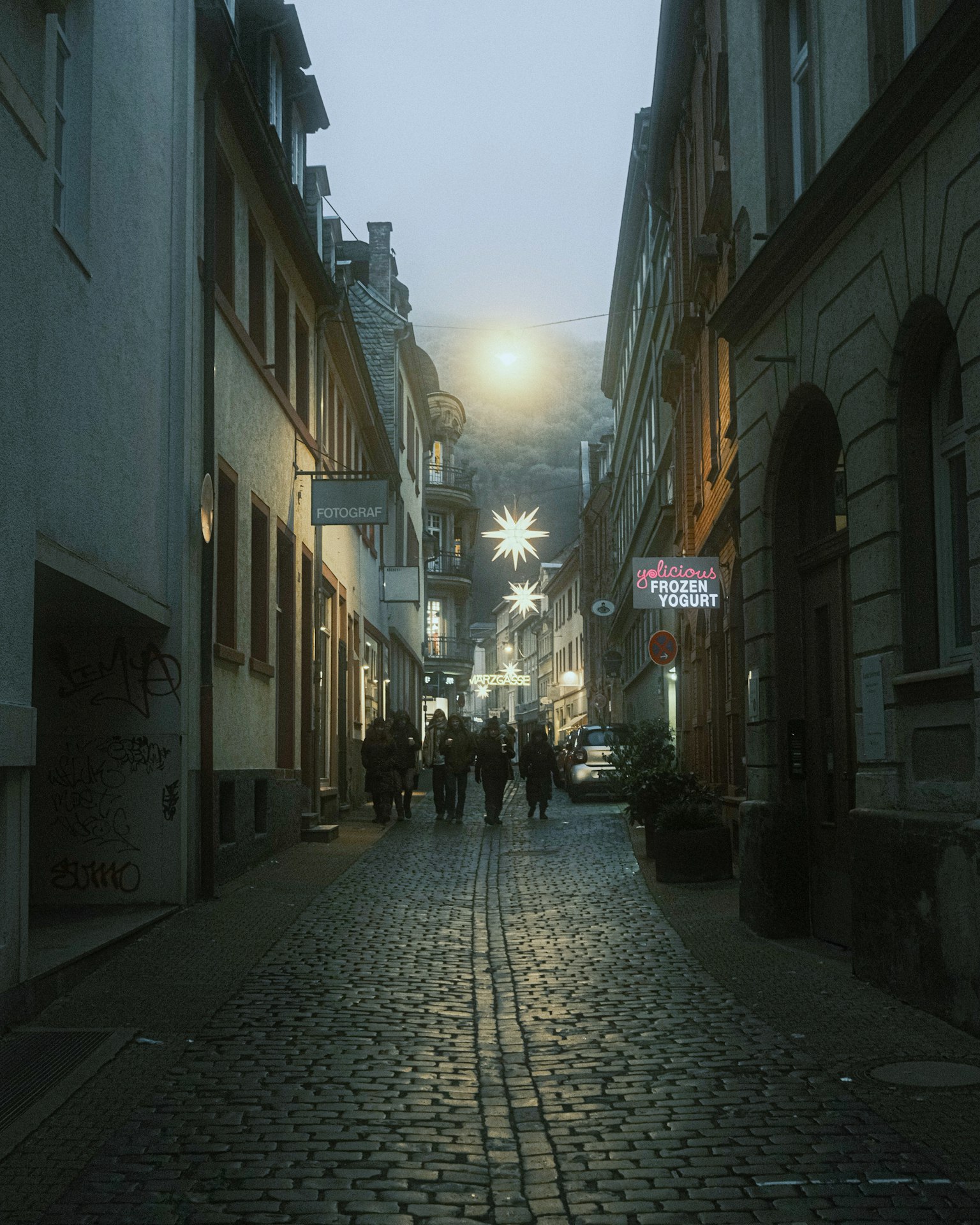 People walking along a cobblestone street in the fog