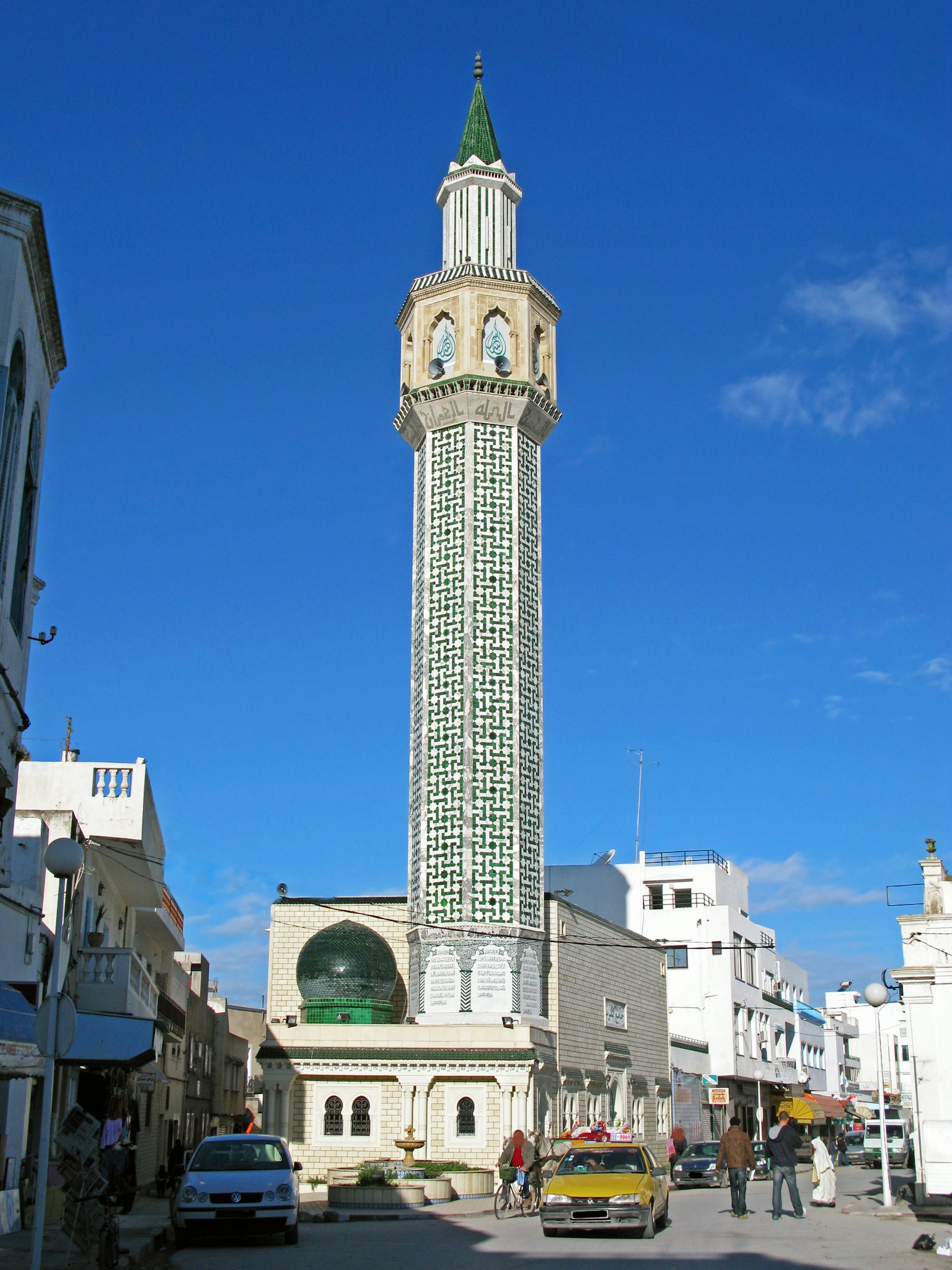 Alto minareto di una moschea circondato da edifici bianchi sotto un cielo blu