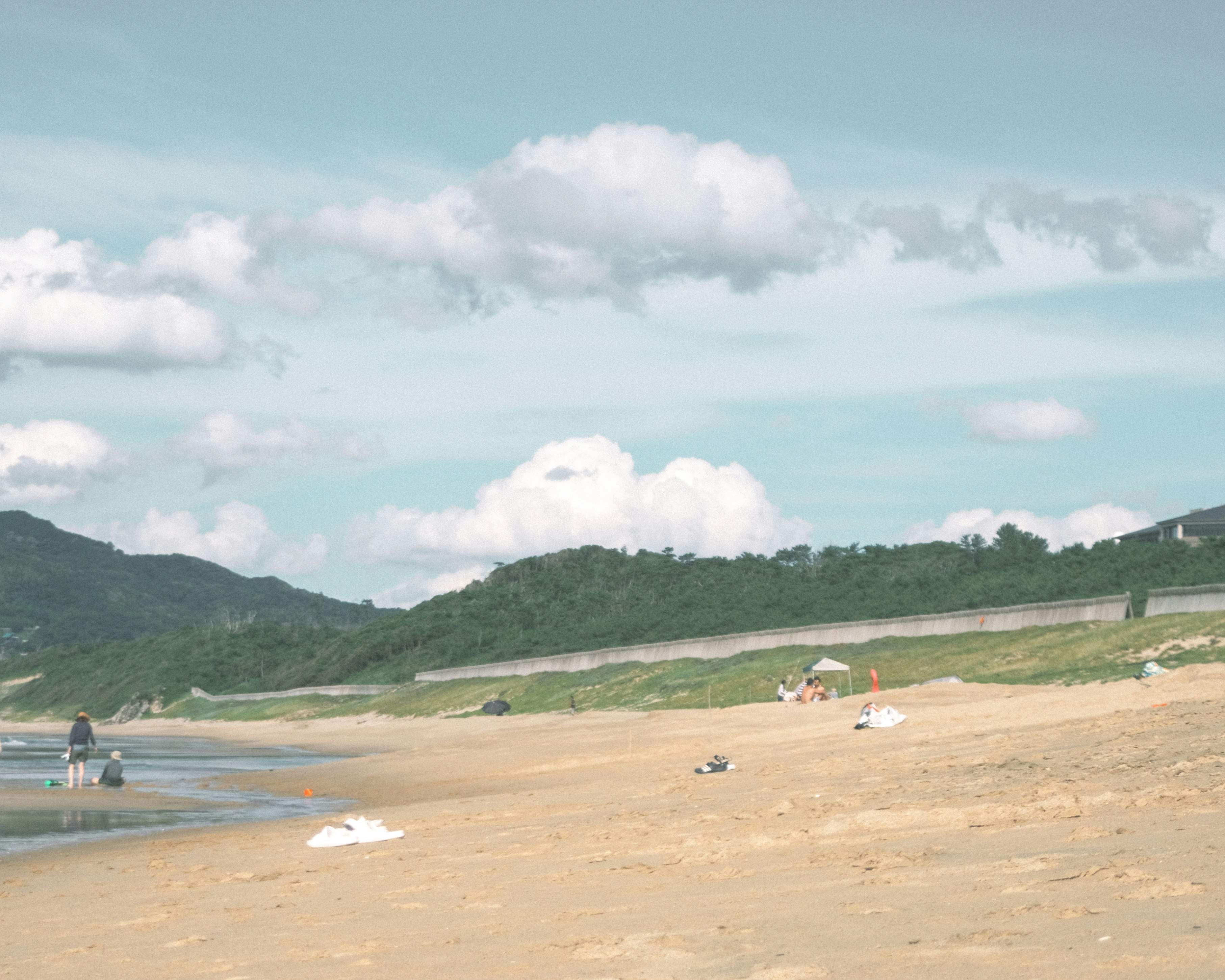 A sandy beach with distant green hills under a partly cloudy sky