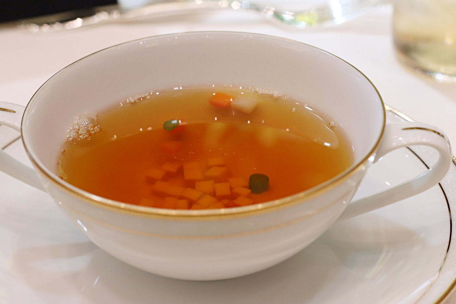 Soupe claire dans une tasse blanche avec des légumes colorés flottants