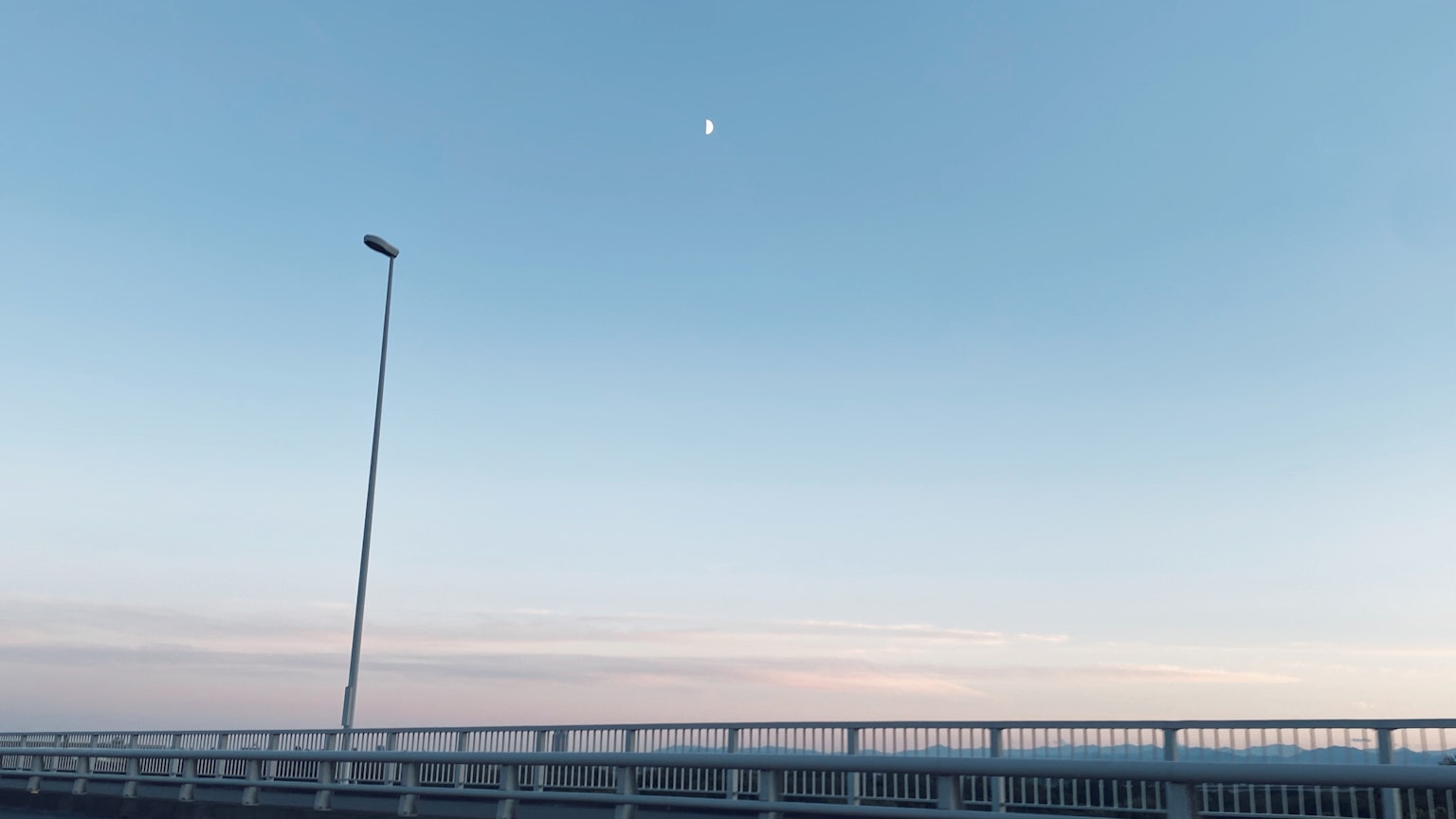 Vista della luna in un cielo blu sopra un lungo ponte