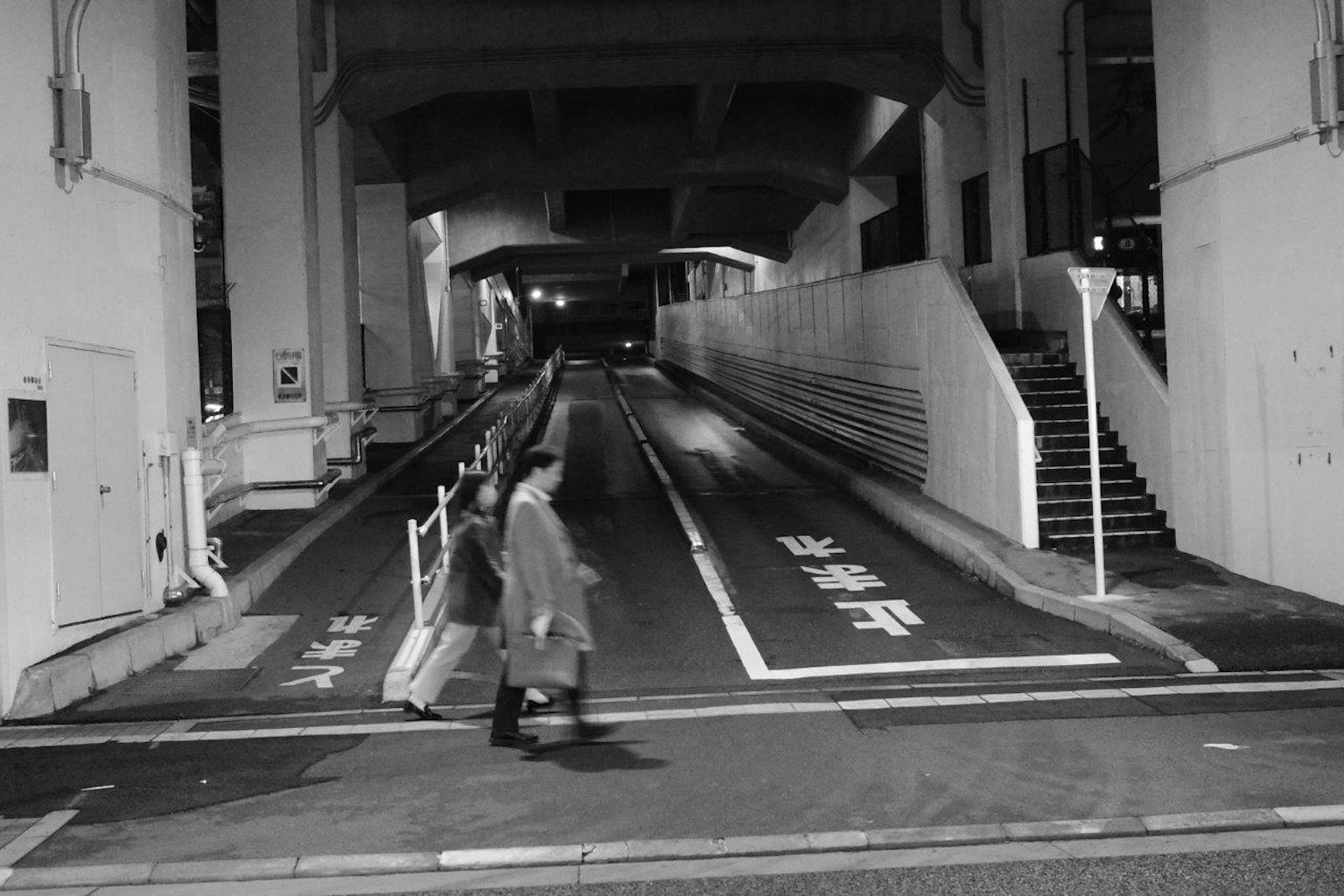 Orang-orang berjalan di kota di malam hari di bawah jembatan beton