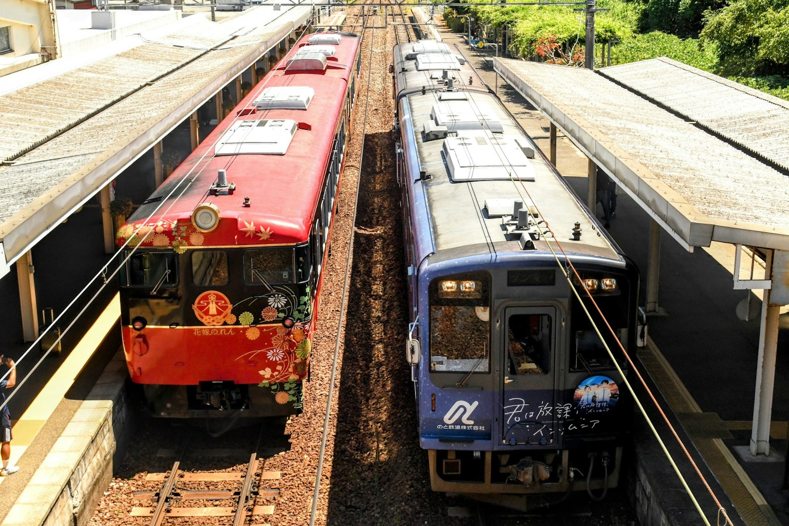 Kereta merah dan biru di stasiun dengan rel terlihat