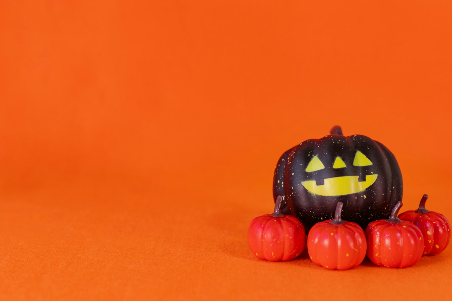 Jack-o'-lantern nera con faccia gialla circondata da piccole zucche rosse su sfondo arancione